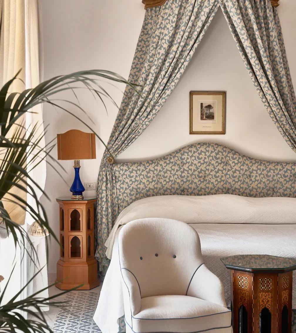 A bed with a woven headboard under a draped canopy, a lamp and a picture on the wall beside it.