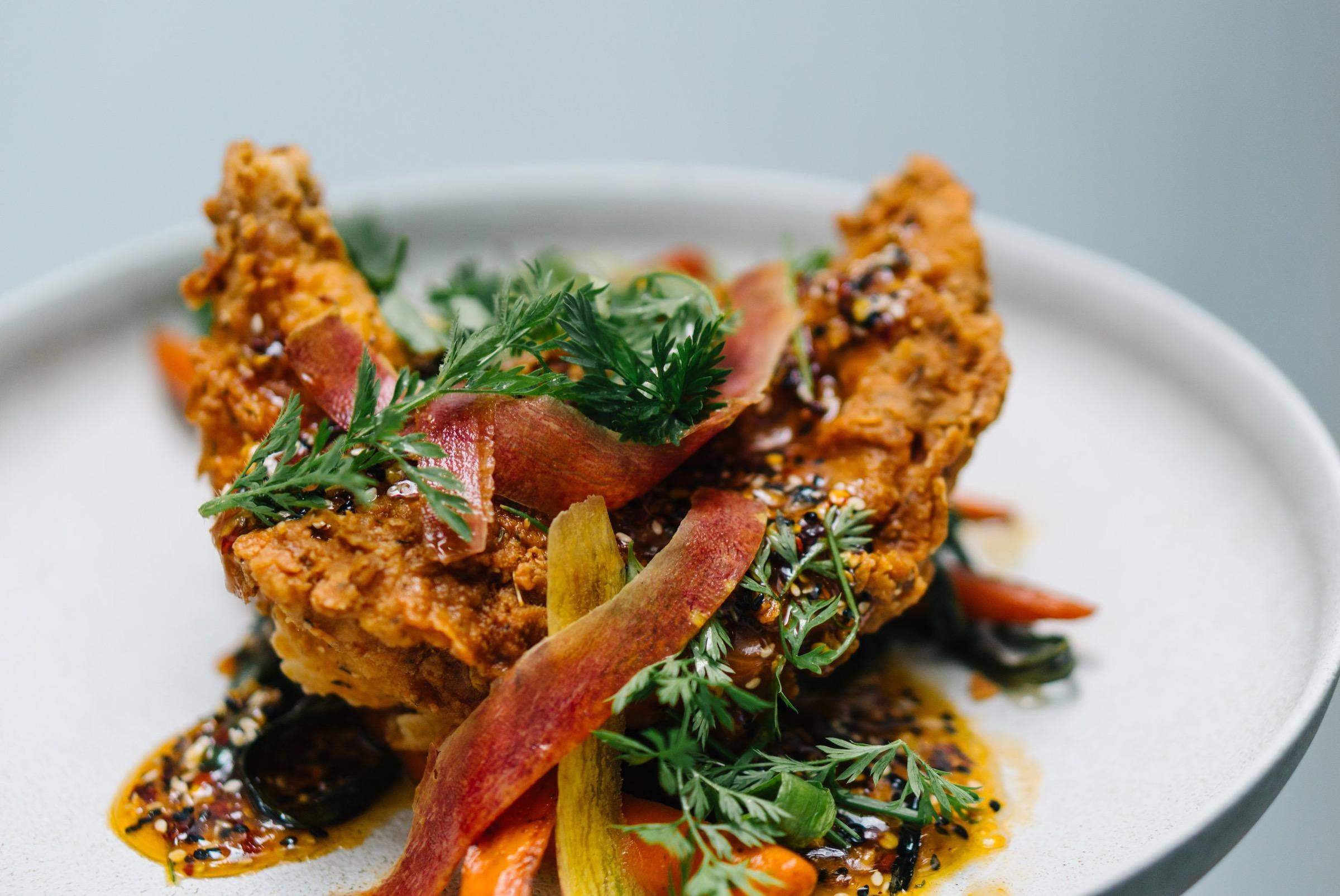 Glazed fried chicken with greens on a white plate