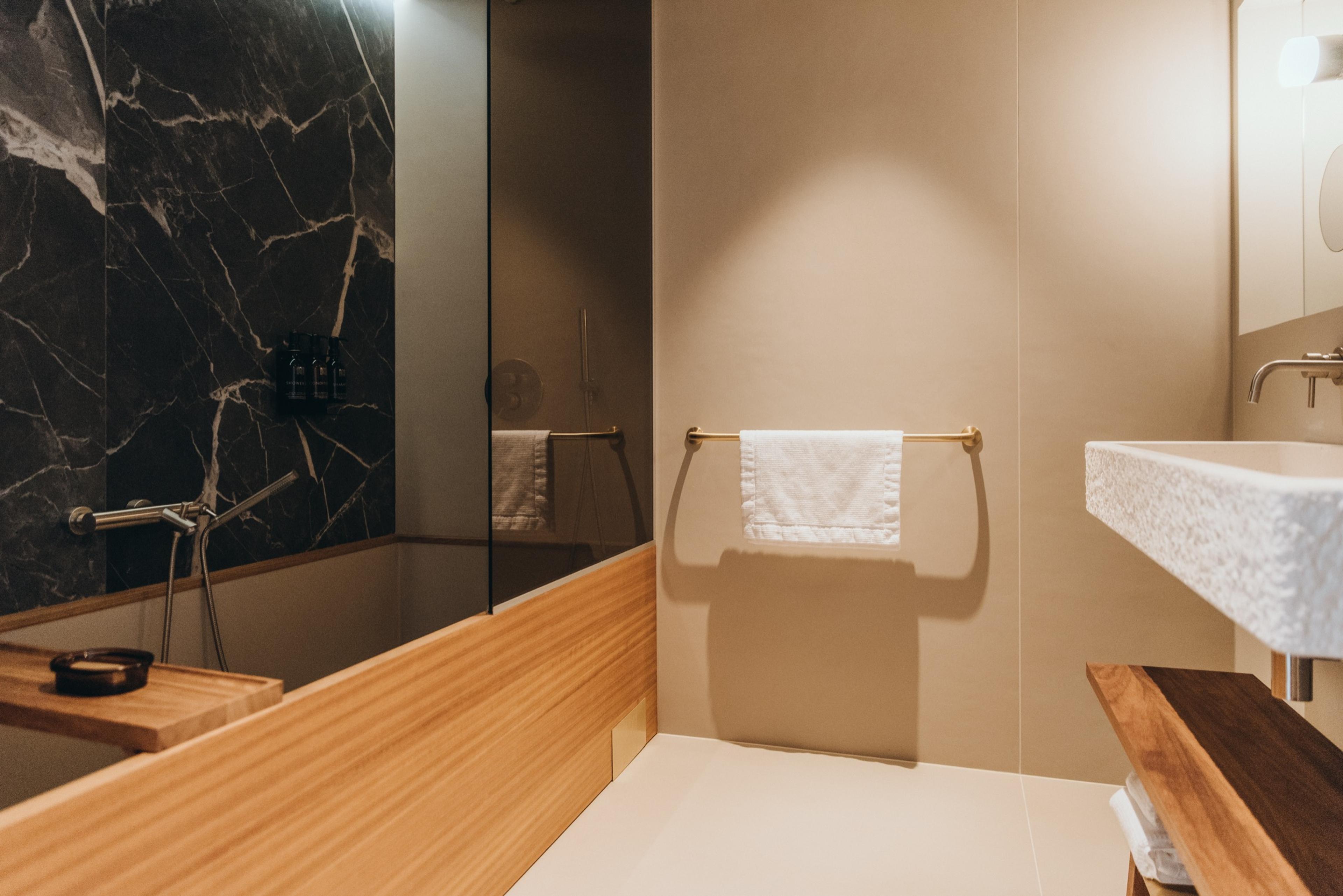 A bathroom with a dark marble wall, a timber-edged bath, and a stone basin on a timber shelf.