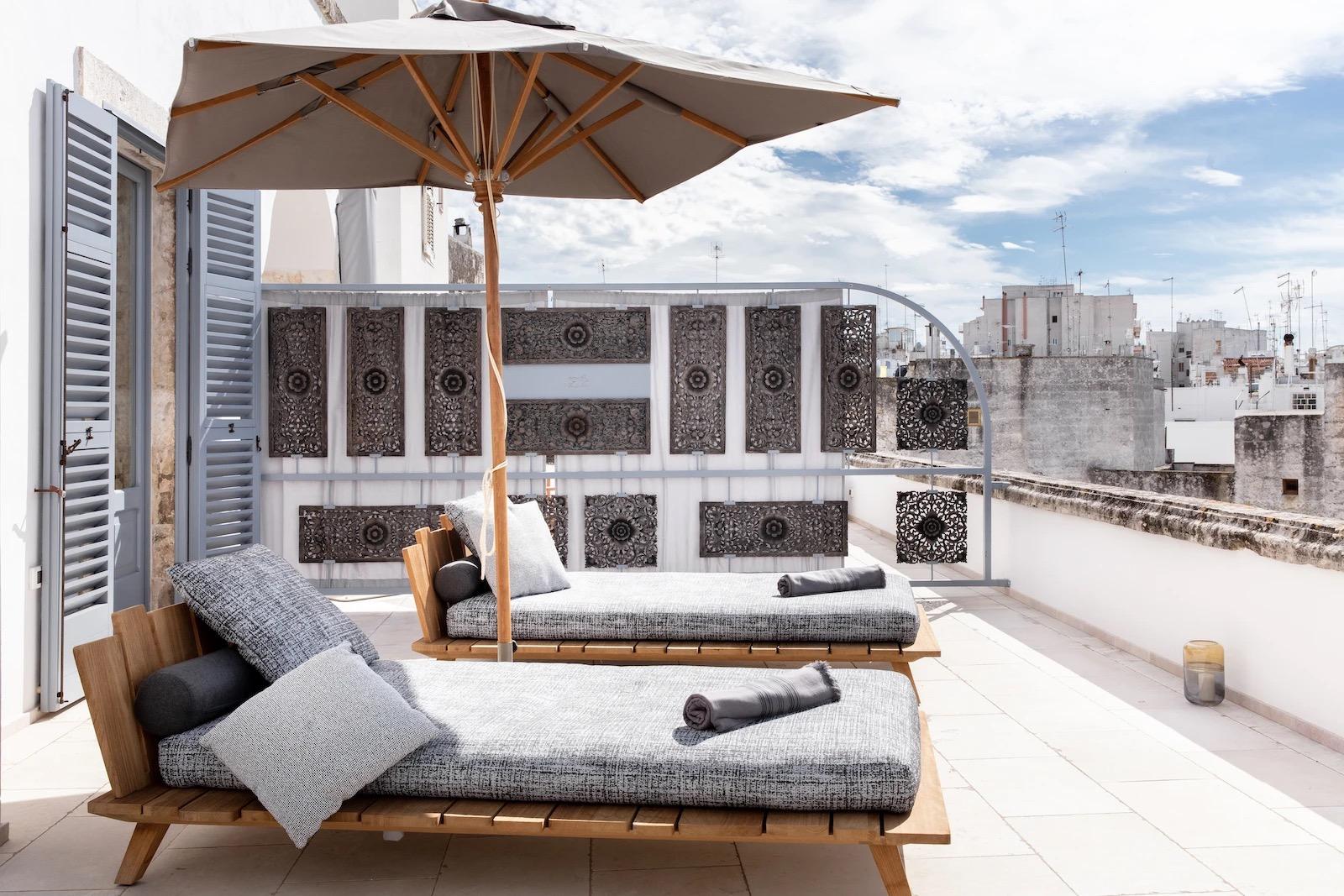 A rooftop terrace with two wooden daybeds under a parasol, carved wooden screens, and the old town's rooftops beyond.