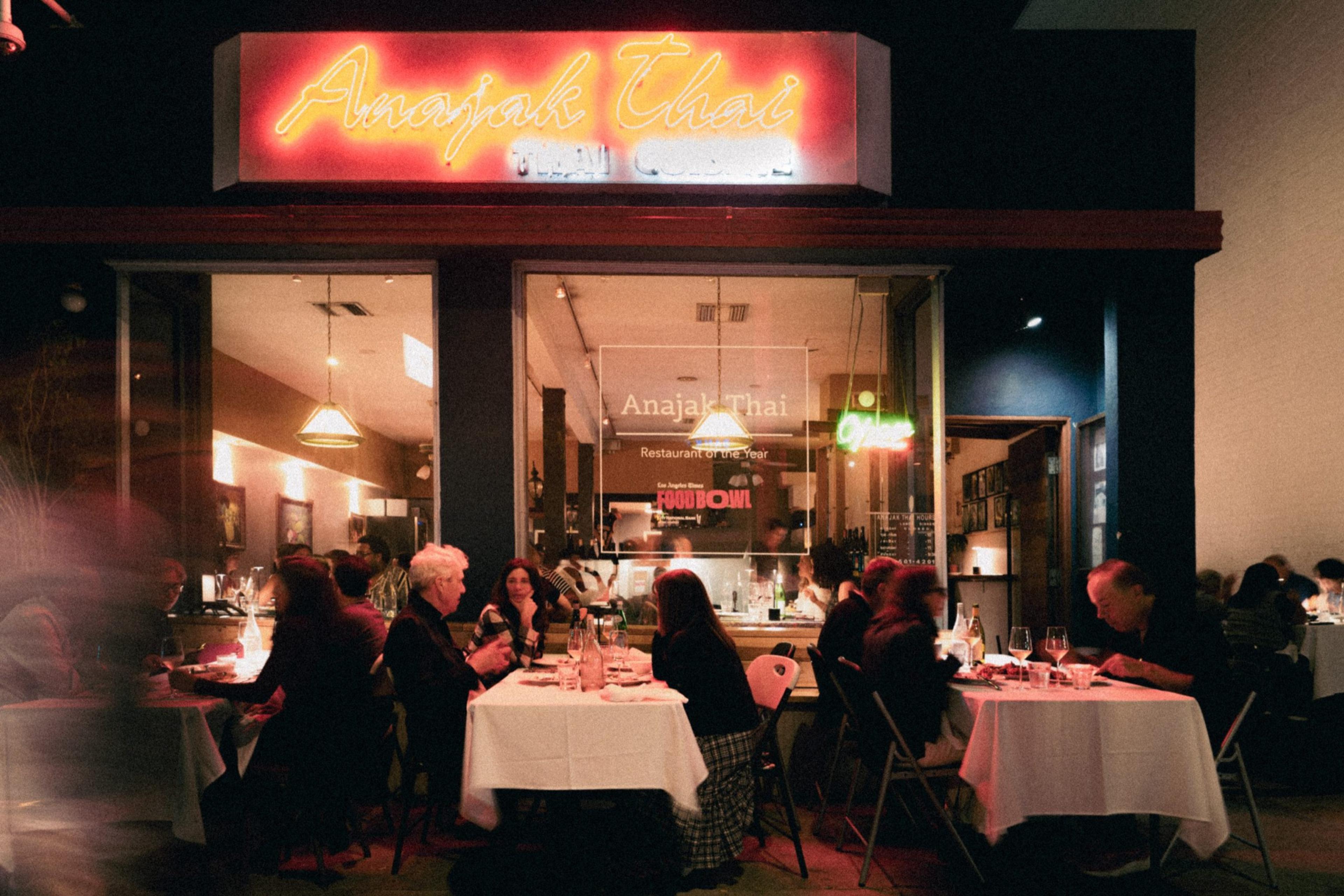 Anajak Thai at night, its neon sign over the window and diners at white-clothed tables inside