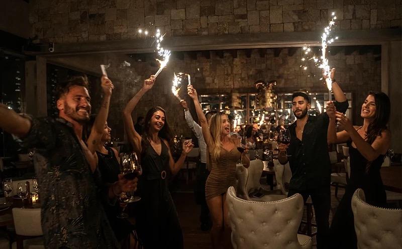 Diners on their feet with sparklers held high in a dark, crowded dining room