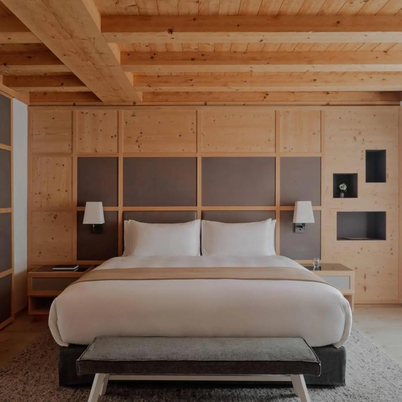 a bedroom with a timber panelled headboard wall, wall mounted lamps either side of a white bed, and a grey bench at its foot