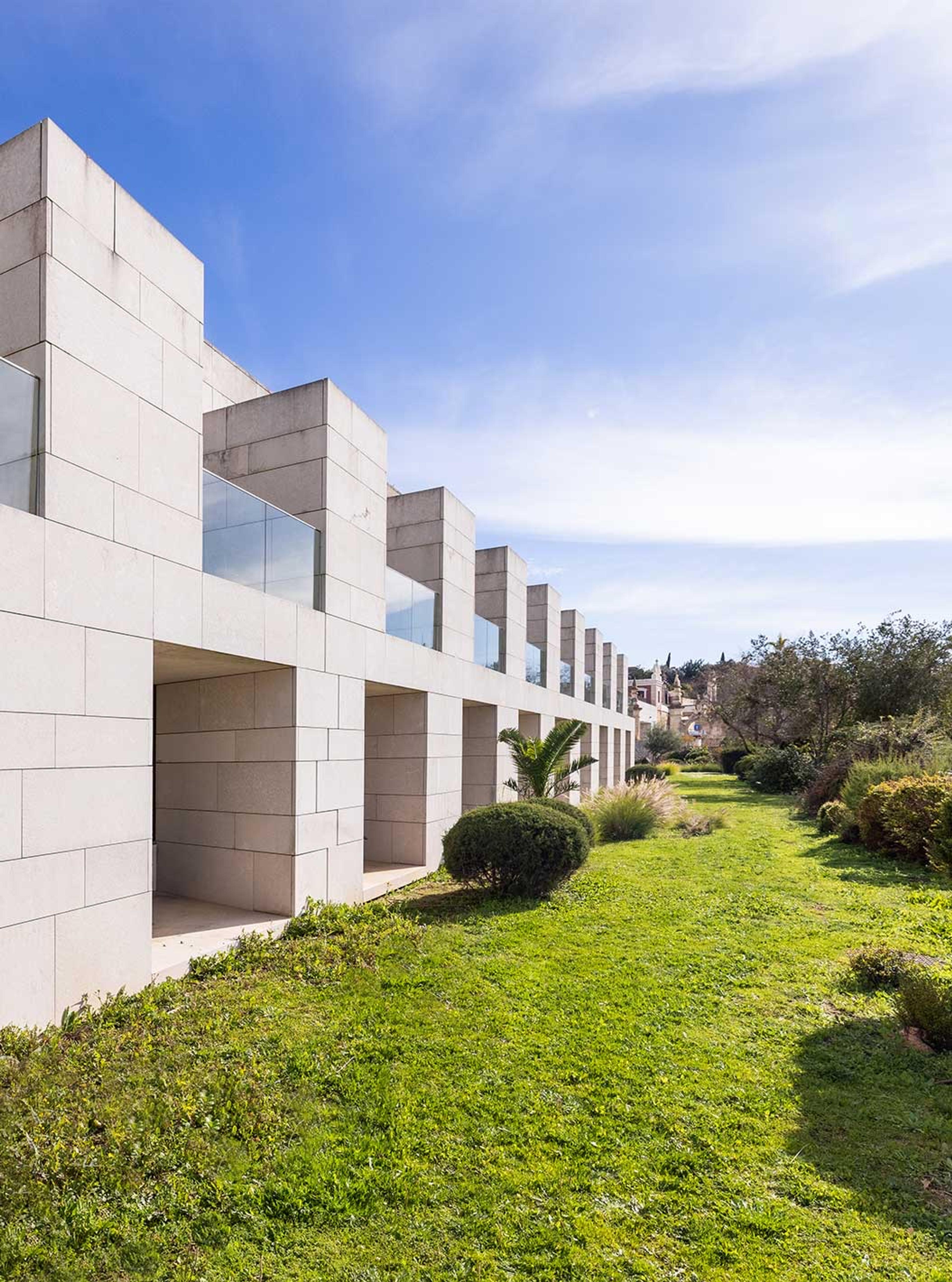 The stone-clad block of guest rooms in daylight, with balconies set into the wall and a grass lawn running alongside it.