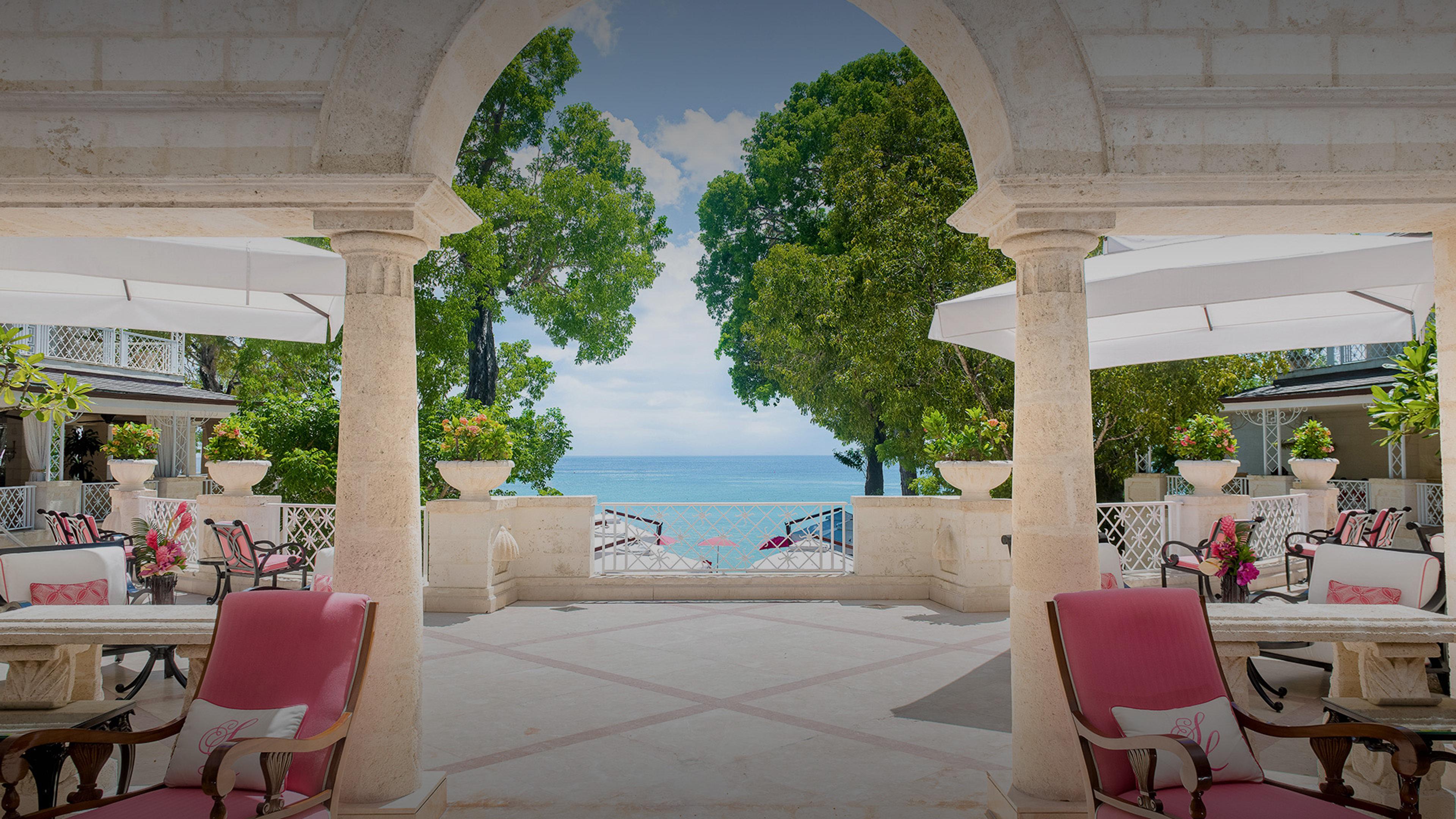 An arched terrace with pink chairs, looking out between the columns to the sea