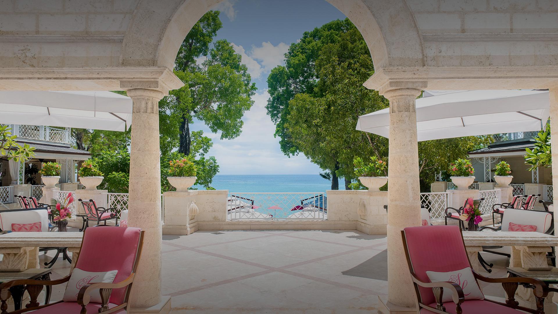 An arched terrace with pink chairs, looking out between the columns to the sea