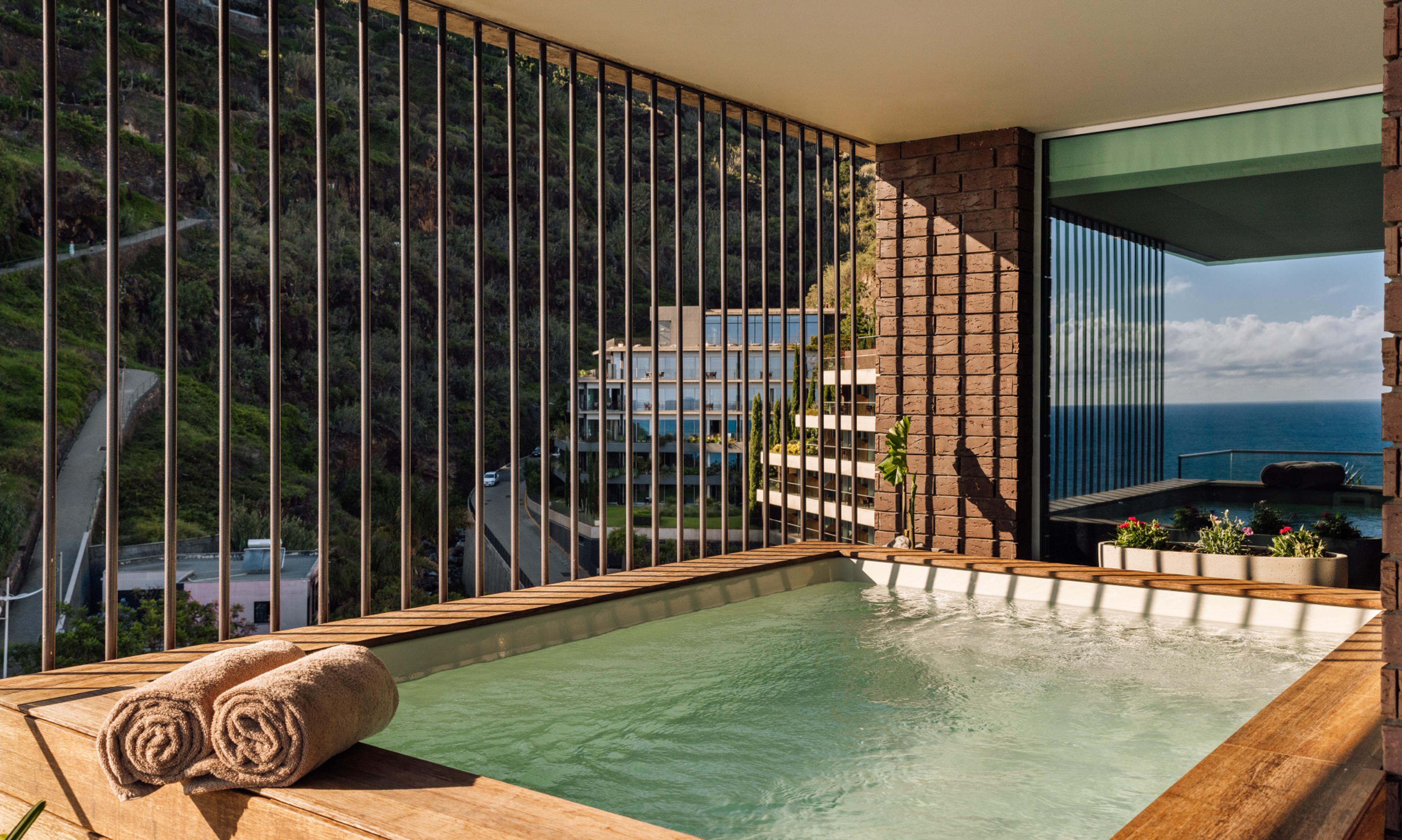 A private plunge pool behind a slatted wooden screen, with the hotel building and the sea in view.