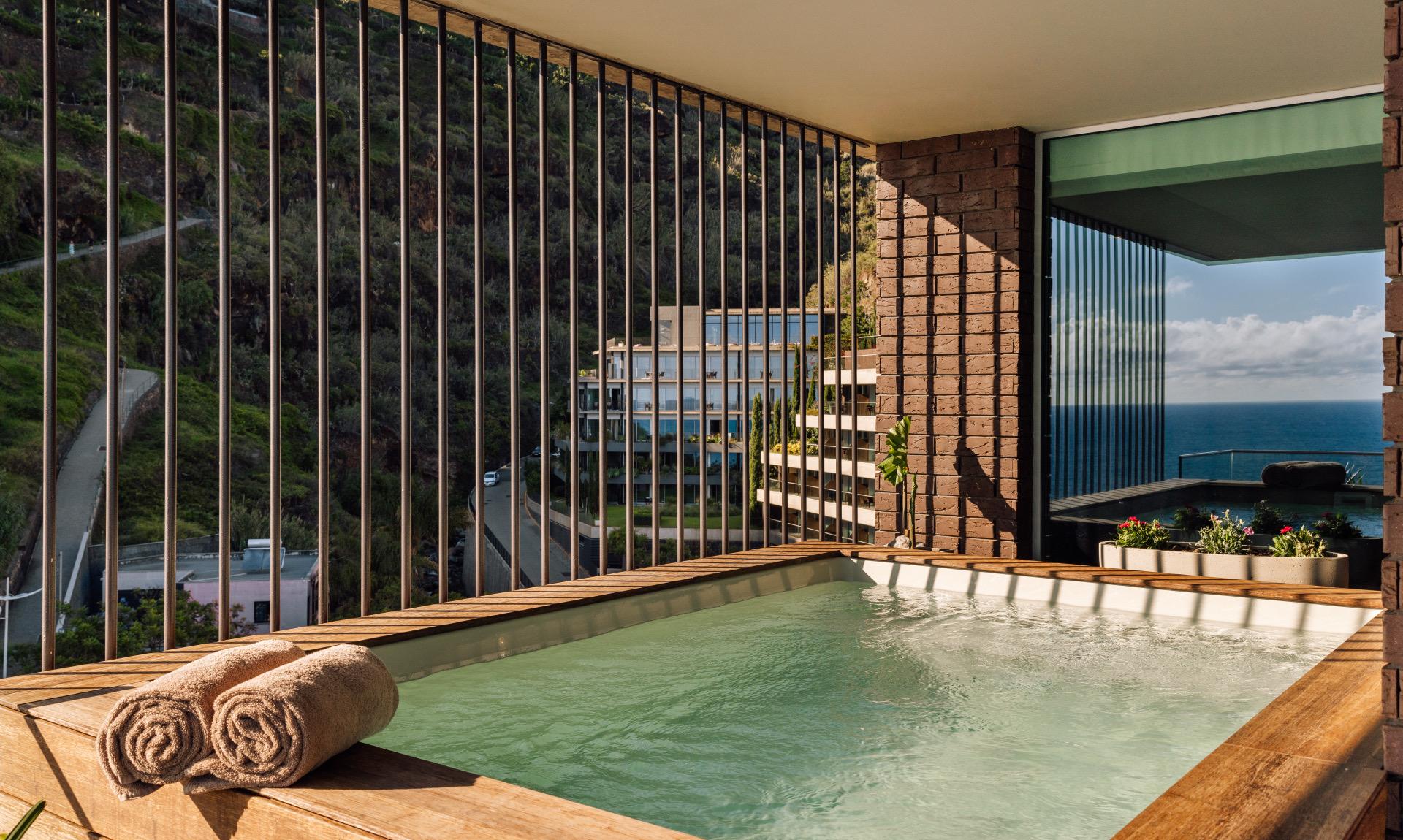 A private plunge pool behind a slatted wooden screen, with the hotel building and the sea in view.