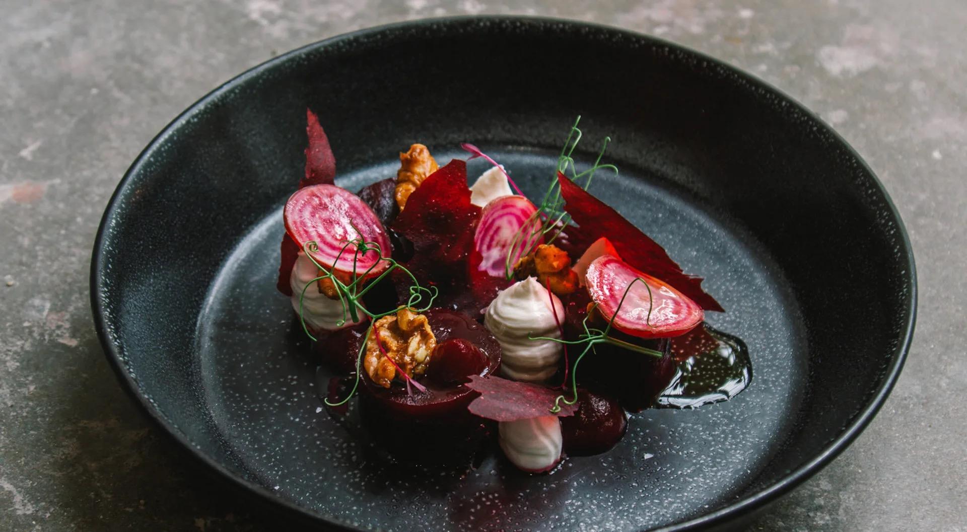 Beetroot and radish slices, walnut pieces, pale quenelles and cress on a dark plate, with a dark sauce pooled beside them.