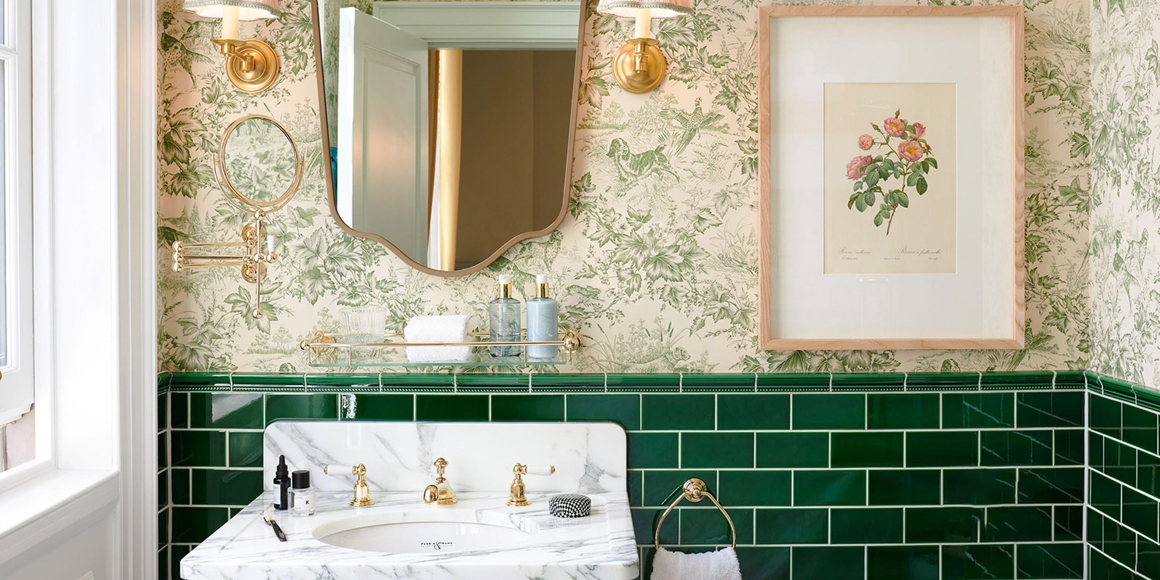 a marble sink with gold taps against green tiled walls, under a scalloped mirror, green wallpaper and a framed botanical print