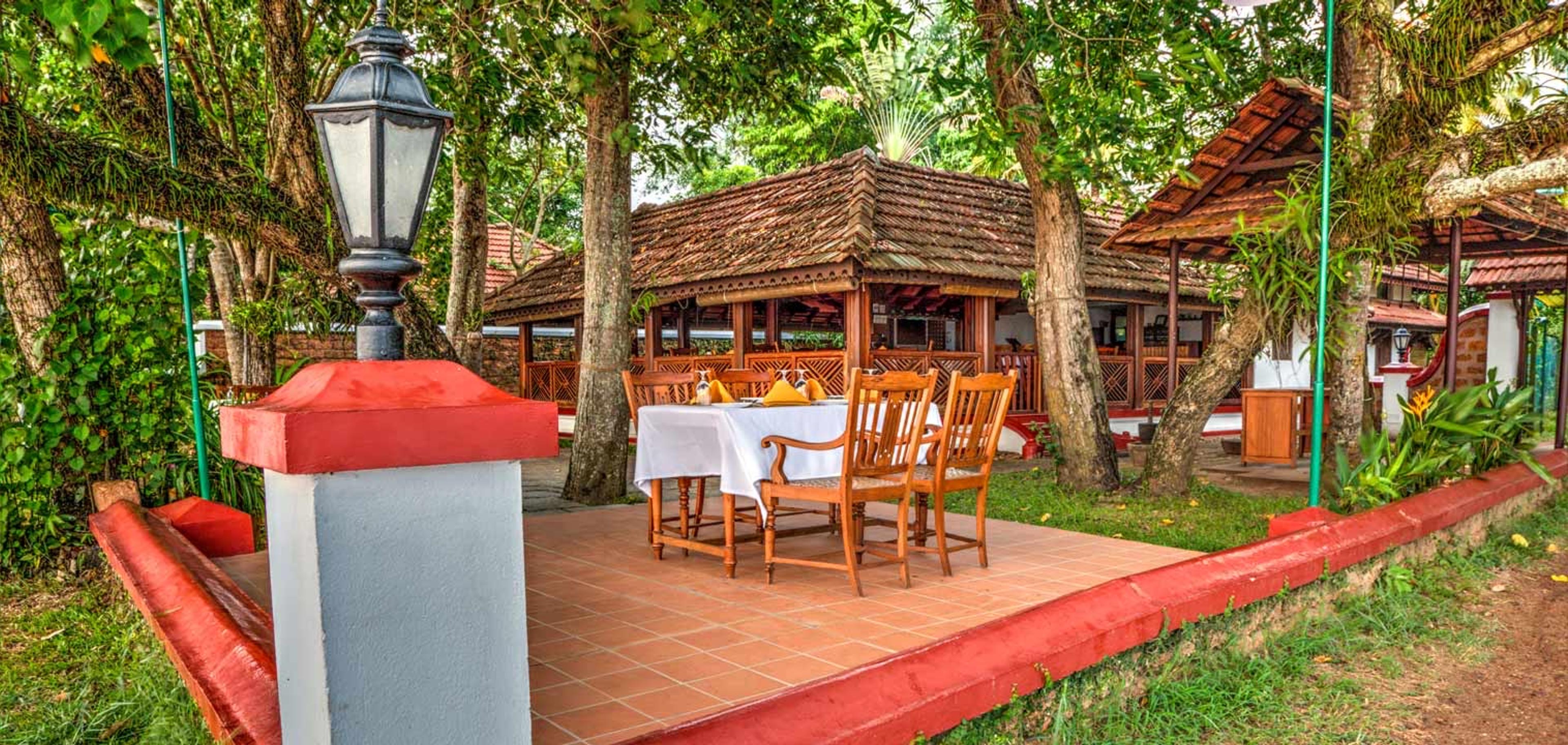 A table set for two beneath trees beside a thatched open sided pavilion