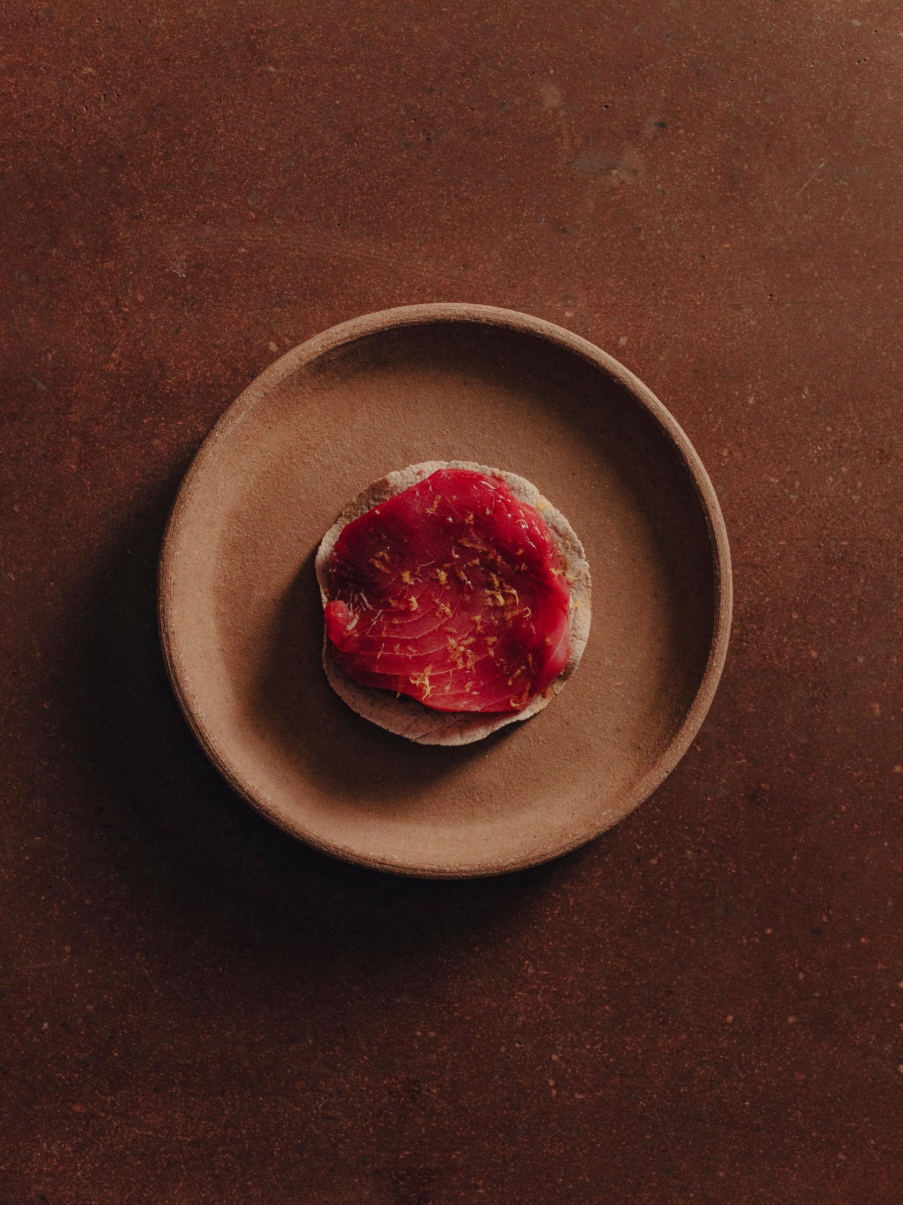 A single dish on a round clay plate against a dark table at Pujol, seen from above