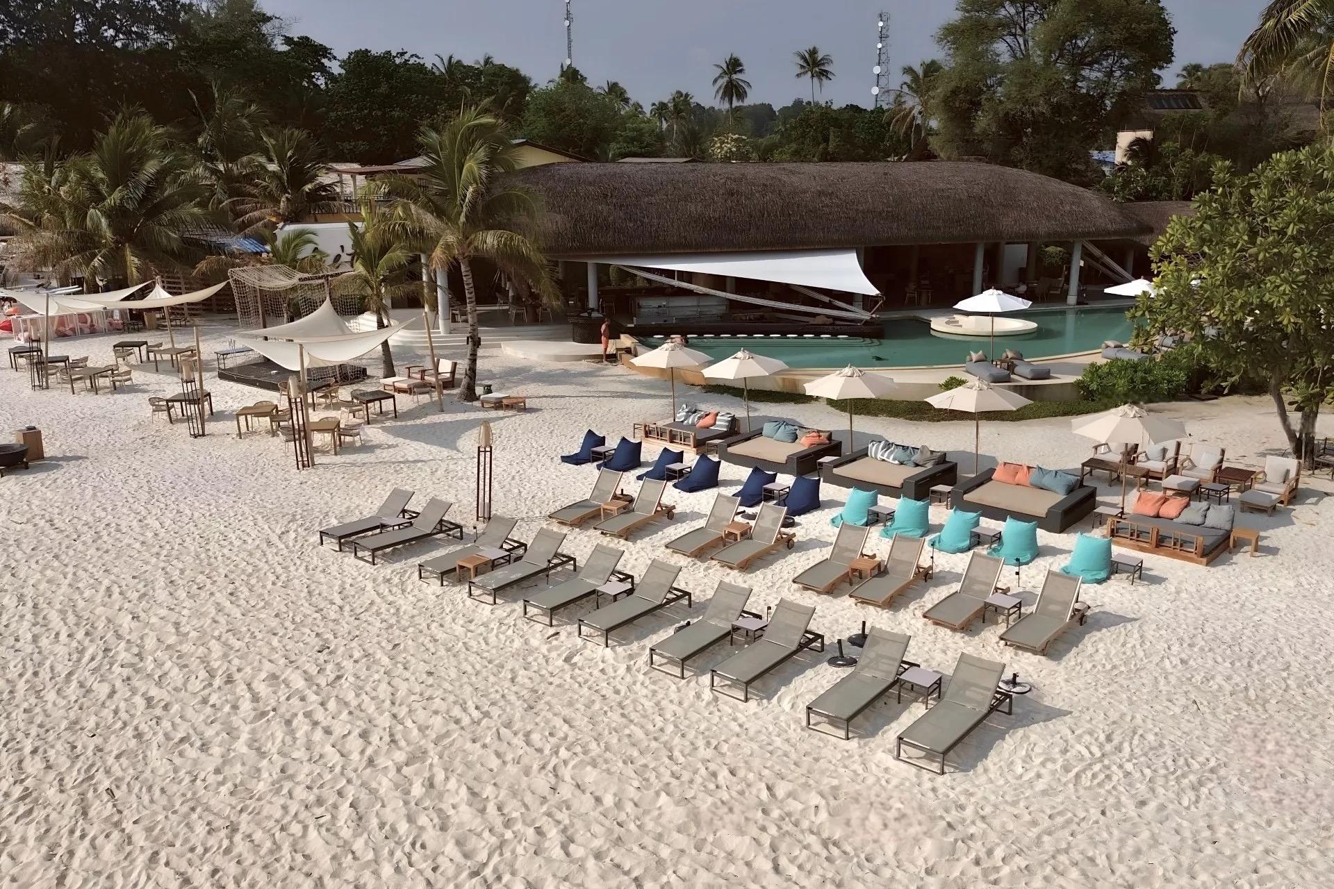 a thatched roof beach pavilion and pool with rows of sunbeds and shaded daybeds set out on white sand