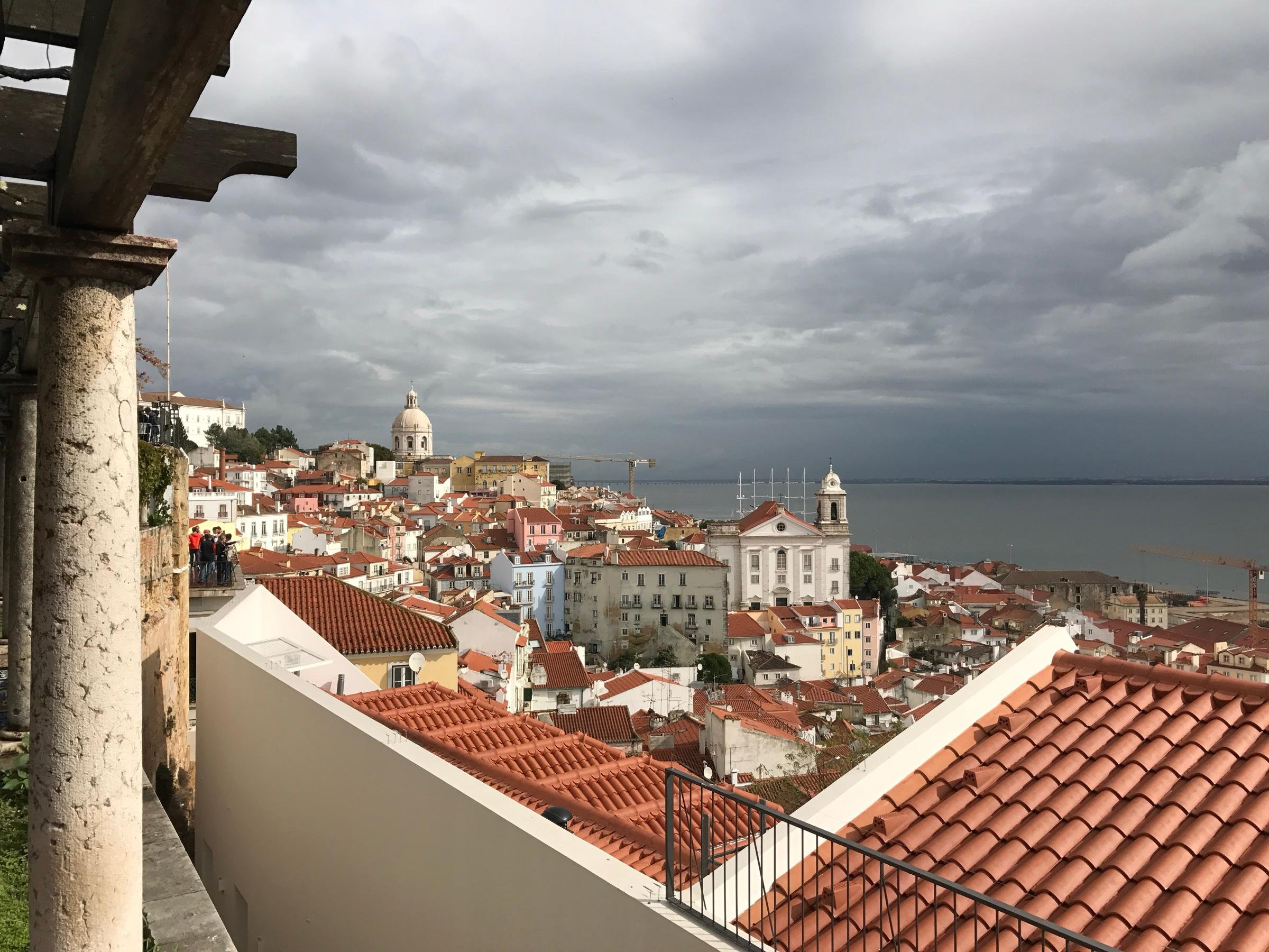 The red-tiled roofs of Alfama falling towards the Tagus, the dome of the National Pantheon on the skyline under a grey sky