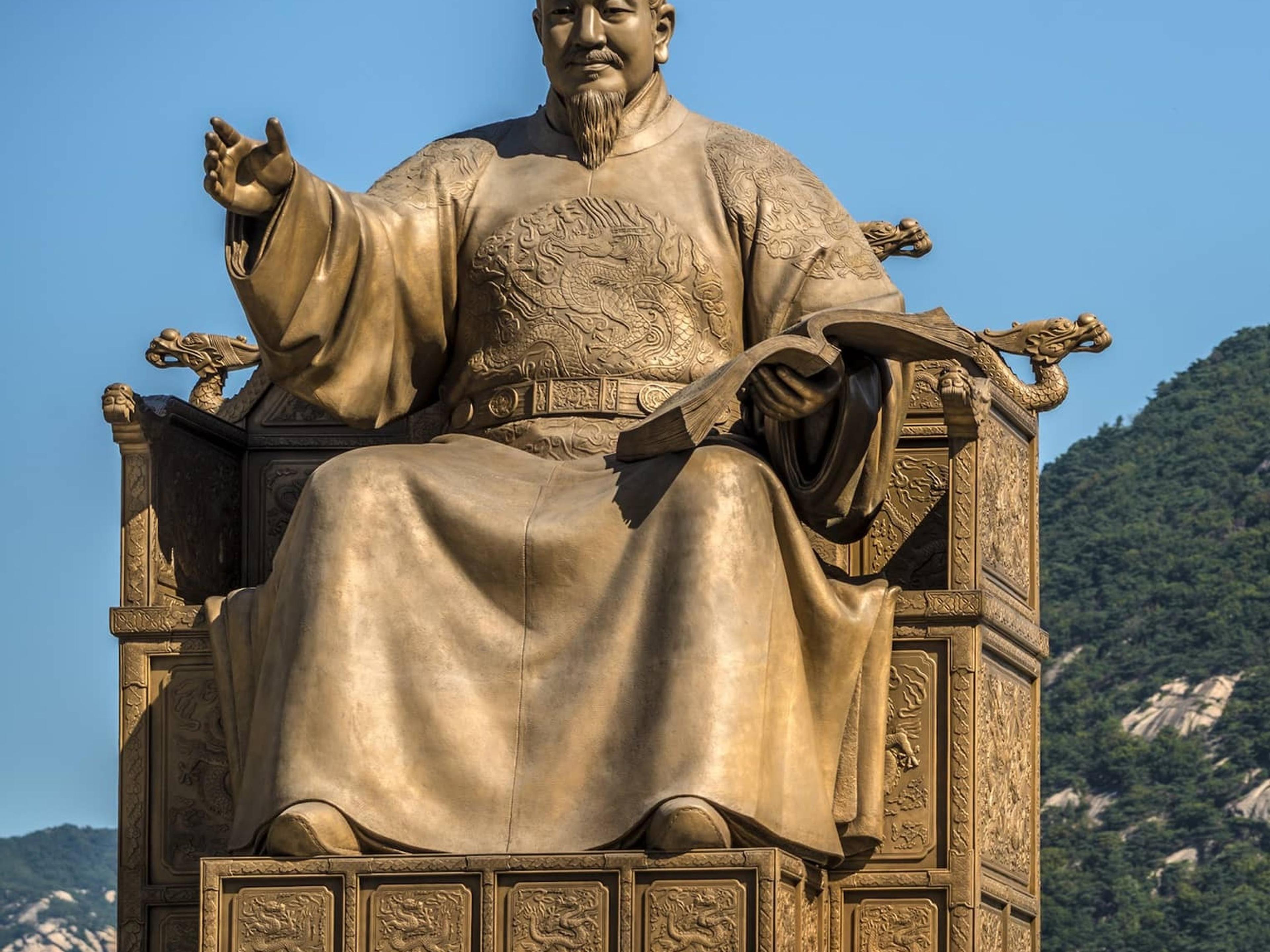 The gilded bronze statue of King Sejong on his throne in Gwanghwamun Square, with a wooded mountain behind
