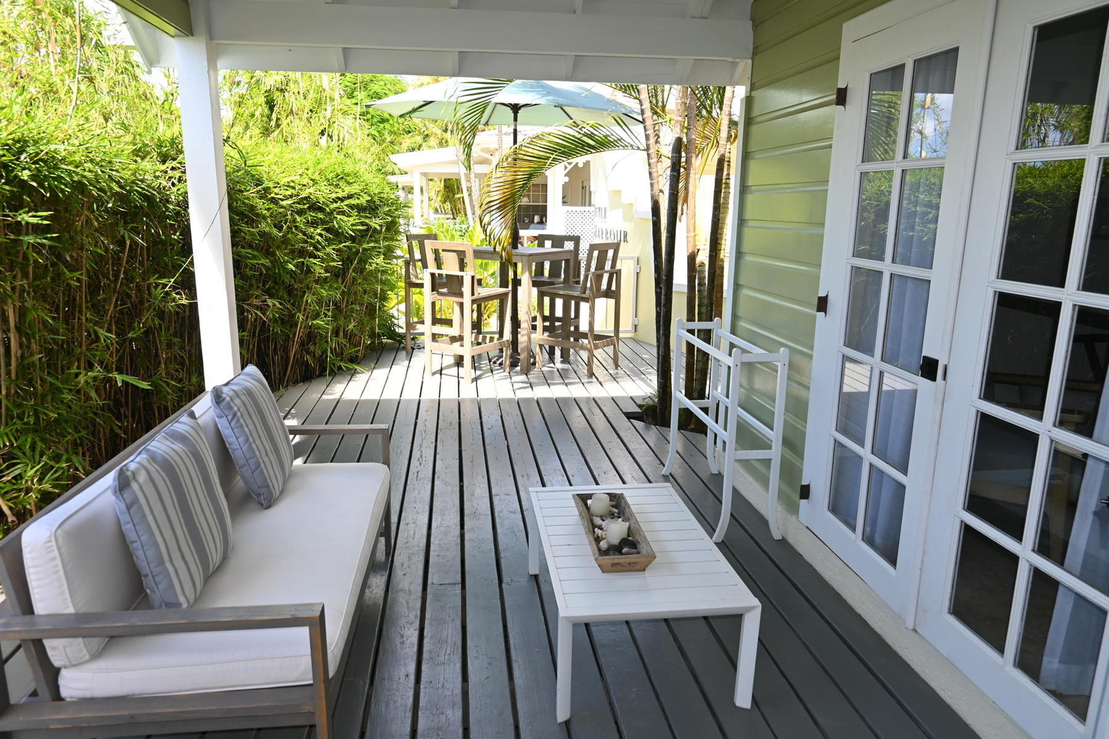 A covered wooden deck with a cushioned bench and coffee table, a bar height table with four chairs and an umbrella beyond.