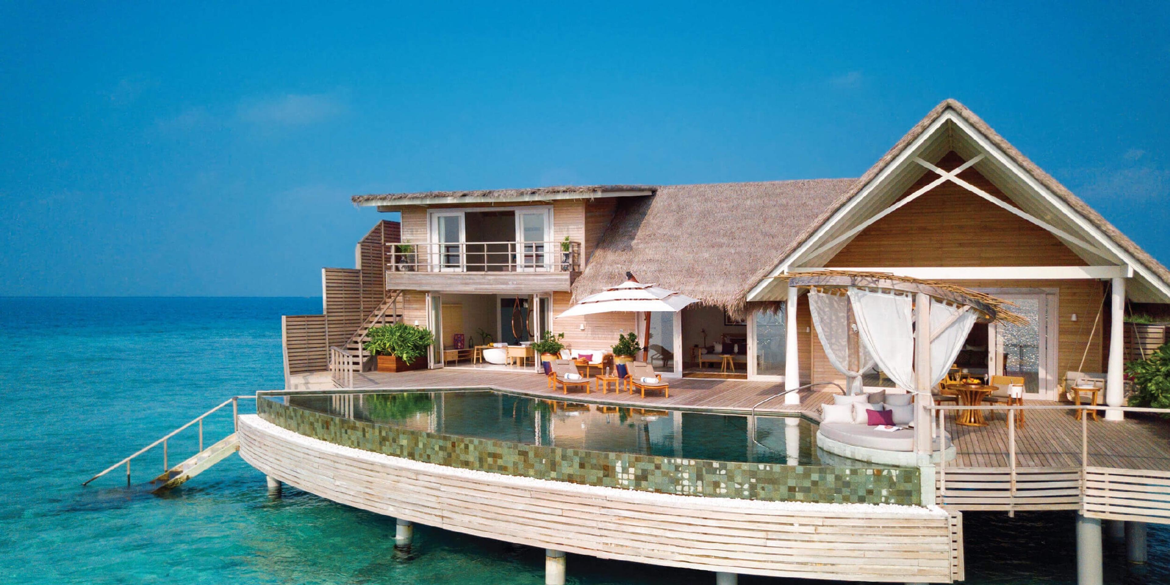 A two-storey overwater villa with a thatched roof, a balcony and a curved pool, built on stilts over the lagoon.