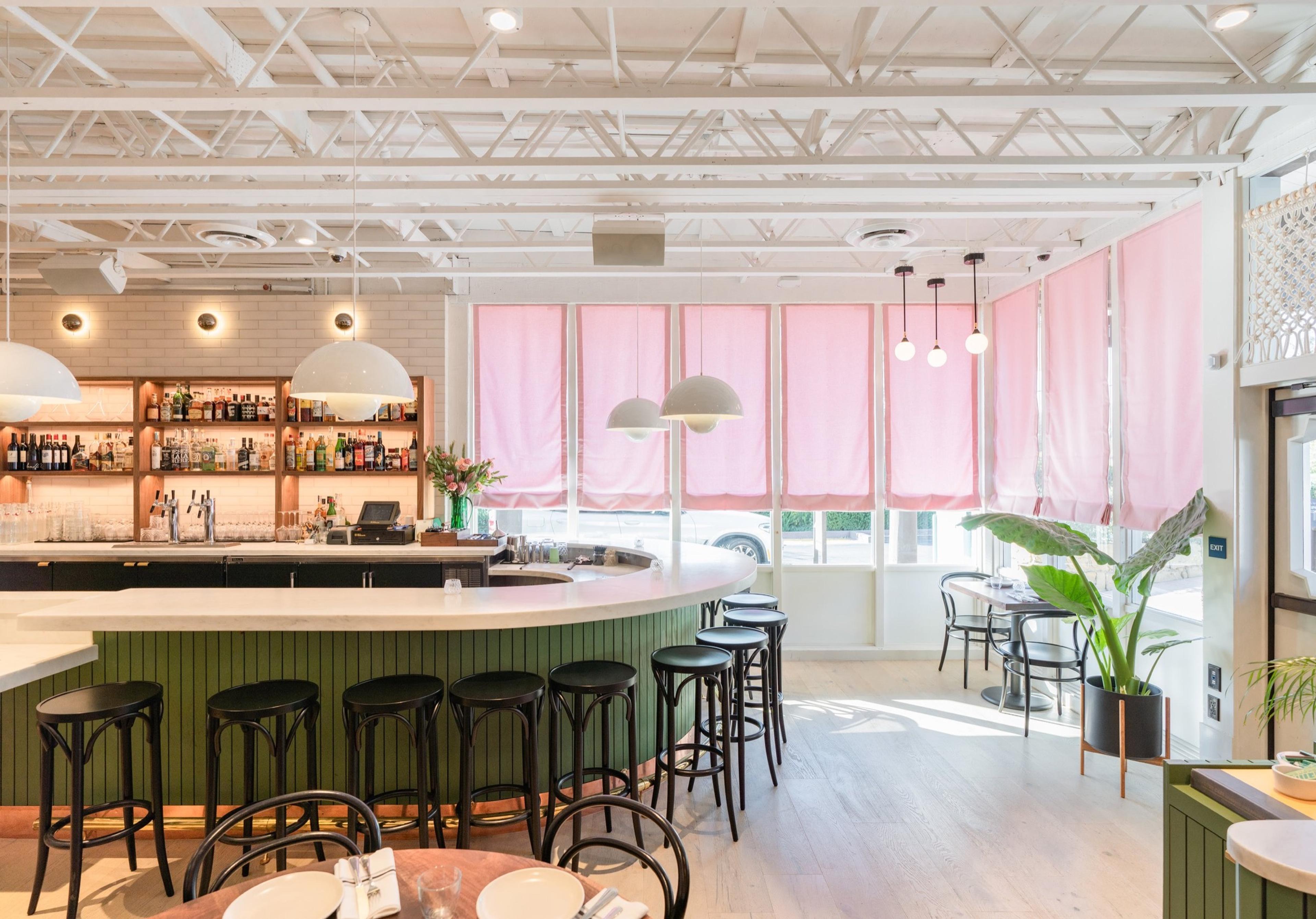 Bettina's dining room, a curved bar with stools under round pendant lights and pink-framed windows