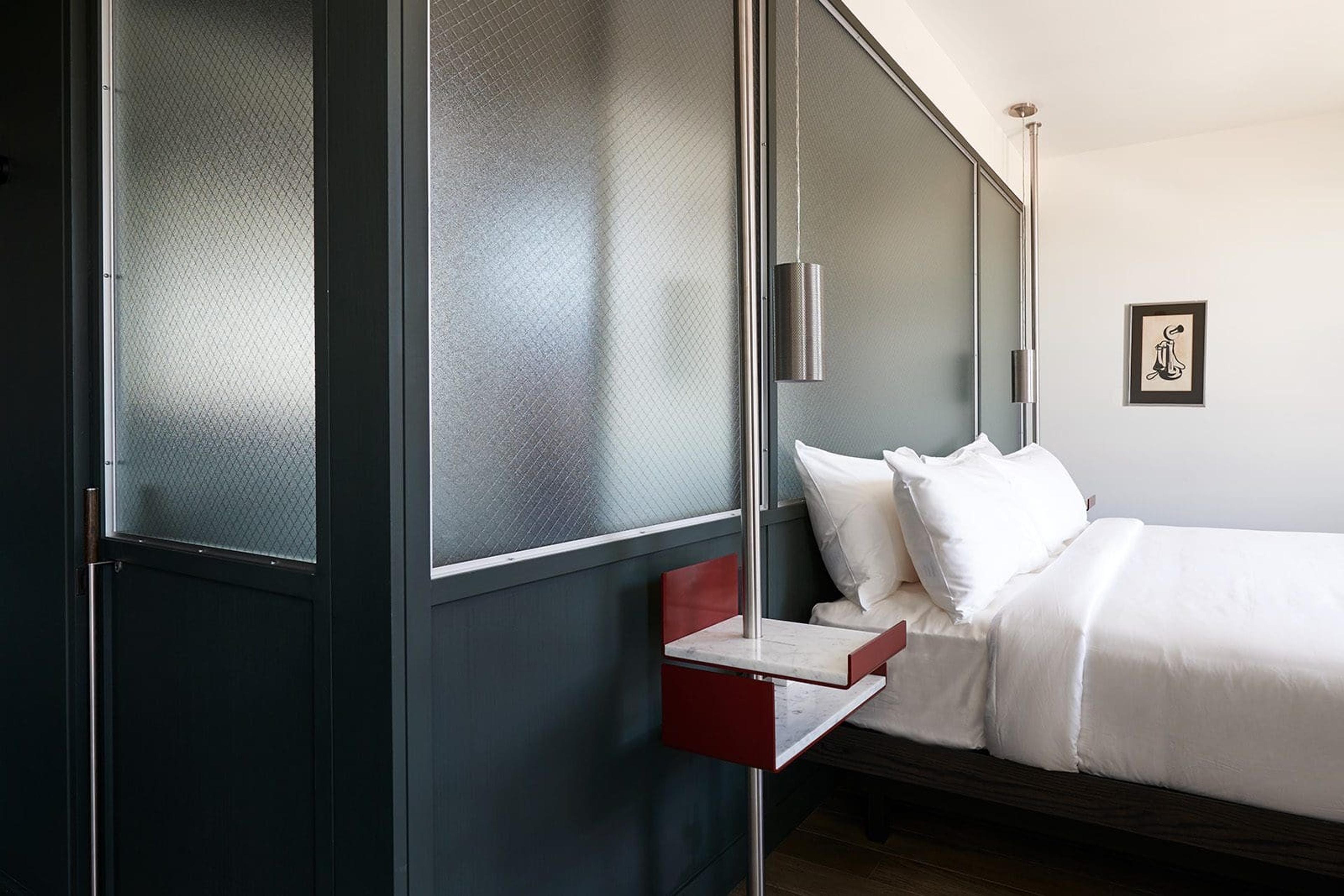 a frosted glass headboard panel in a dark wood frame, a hanging metal pendant light on a pole, a red marble-topped nightstand built into the same pole, and a small framed print on the wall beside the bed