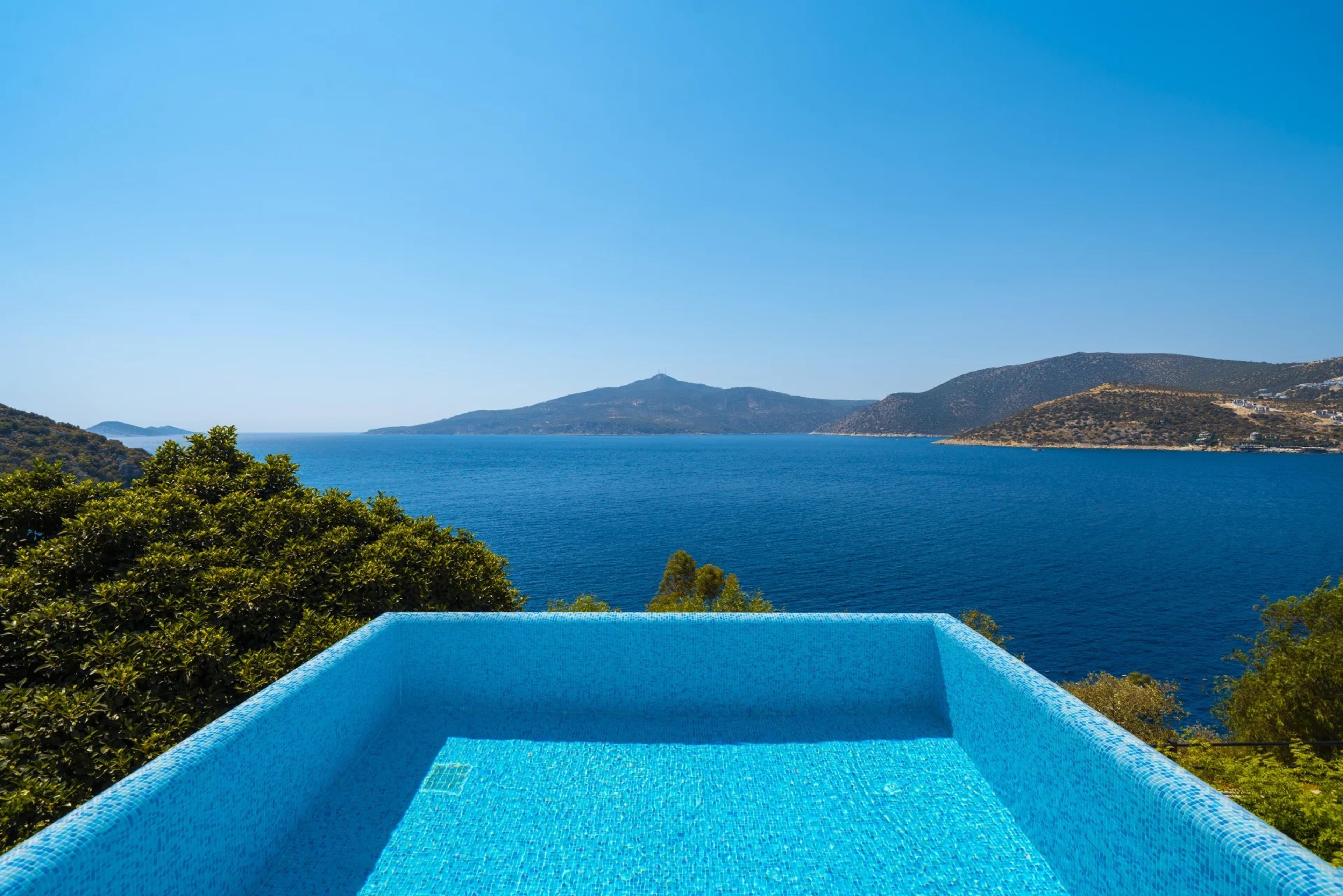 A plunge pool on a rocky ledge, with the sea, a distant island and hills beyond.