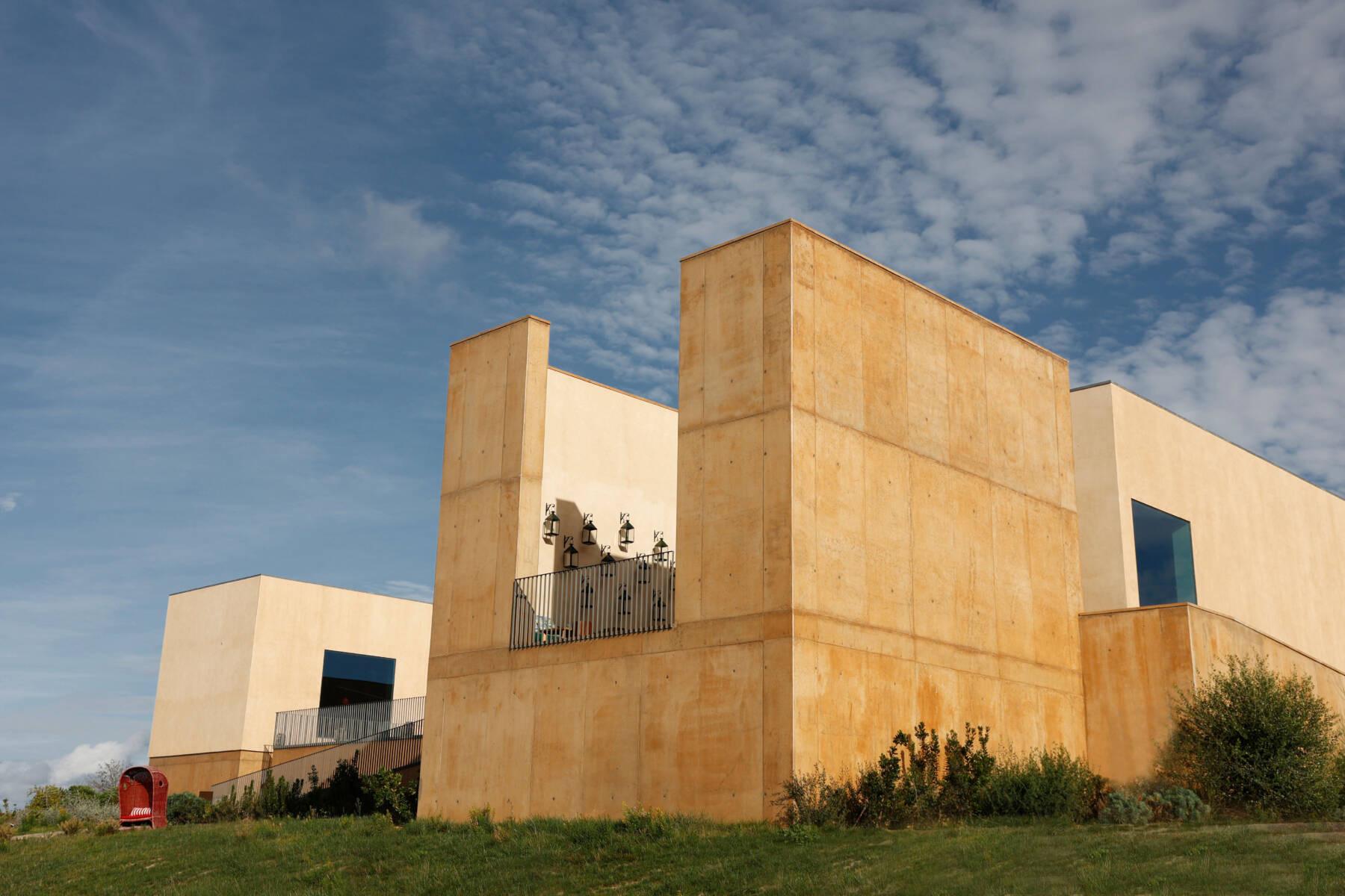The angular render and concrete corner of a building against a blue sky with clouds.