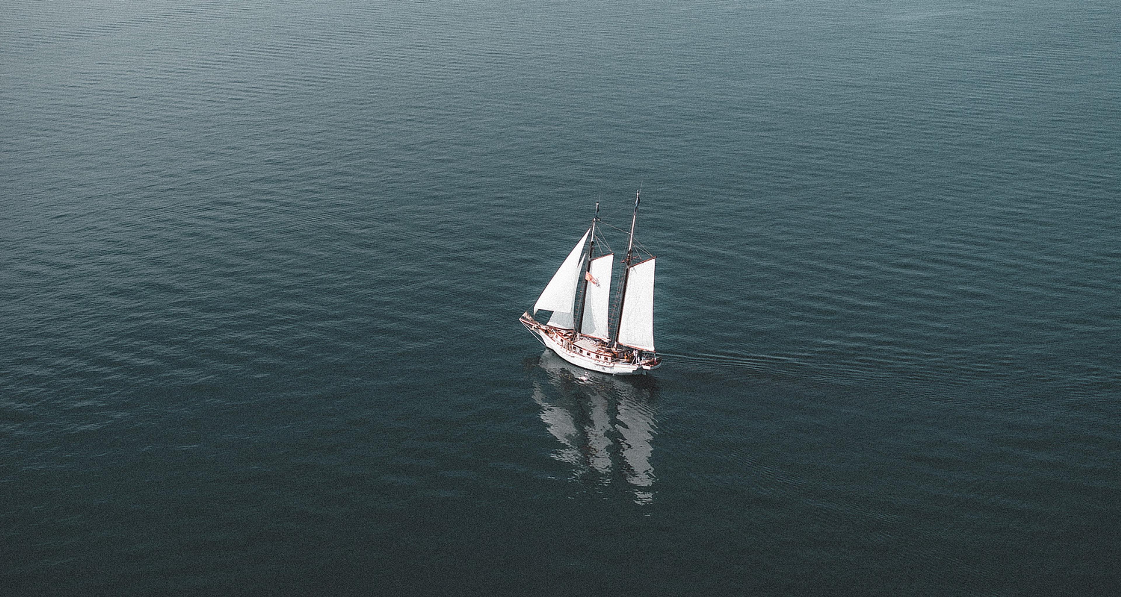 A two-masted sailing boat under white sails on open water.