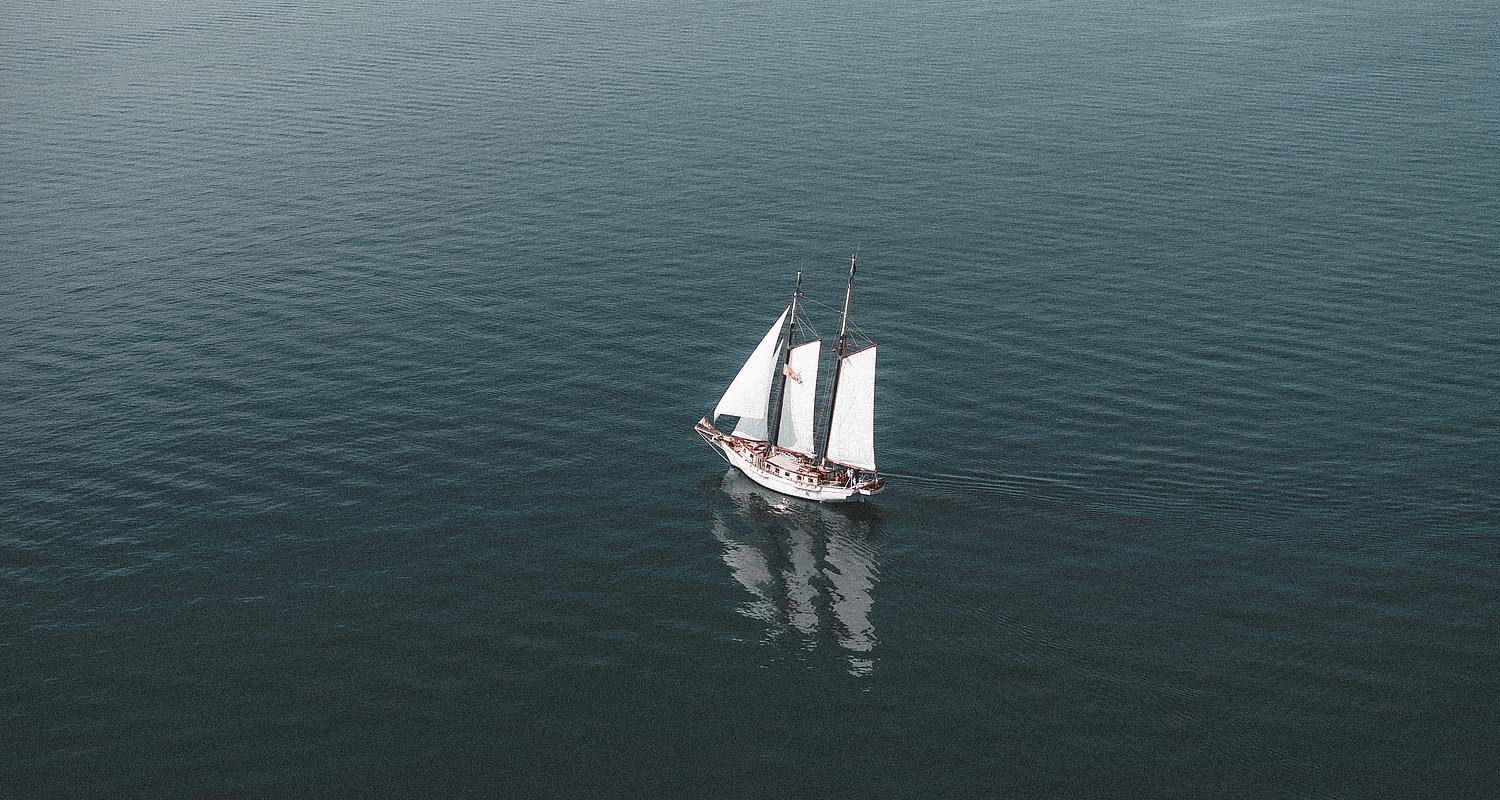 A two-masted sailing boat under white sails on open water.