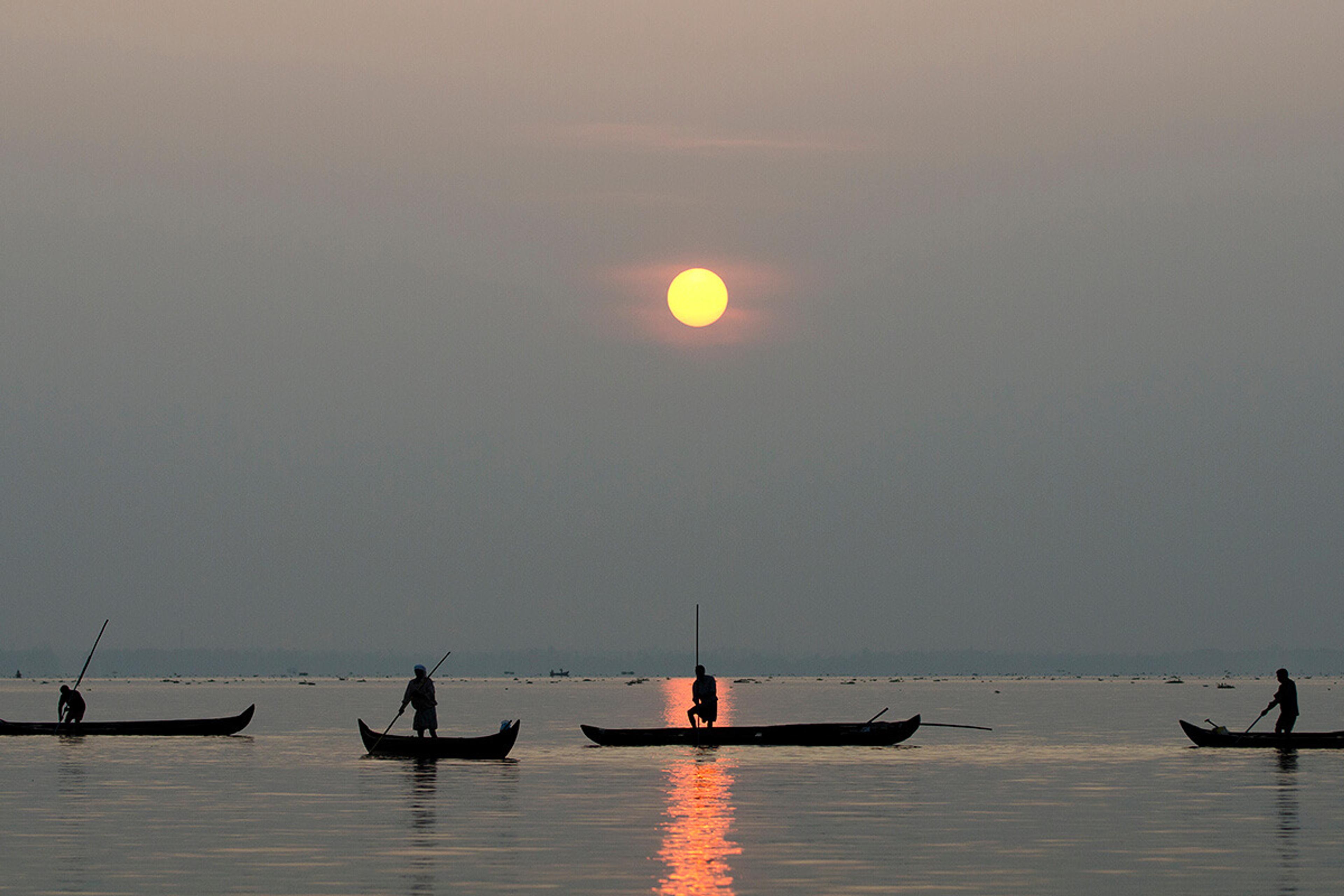 Fishing canoes silhouetted on the lake at sunset, the sun low over the water
