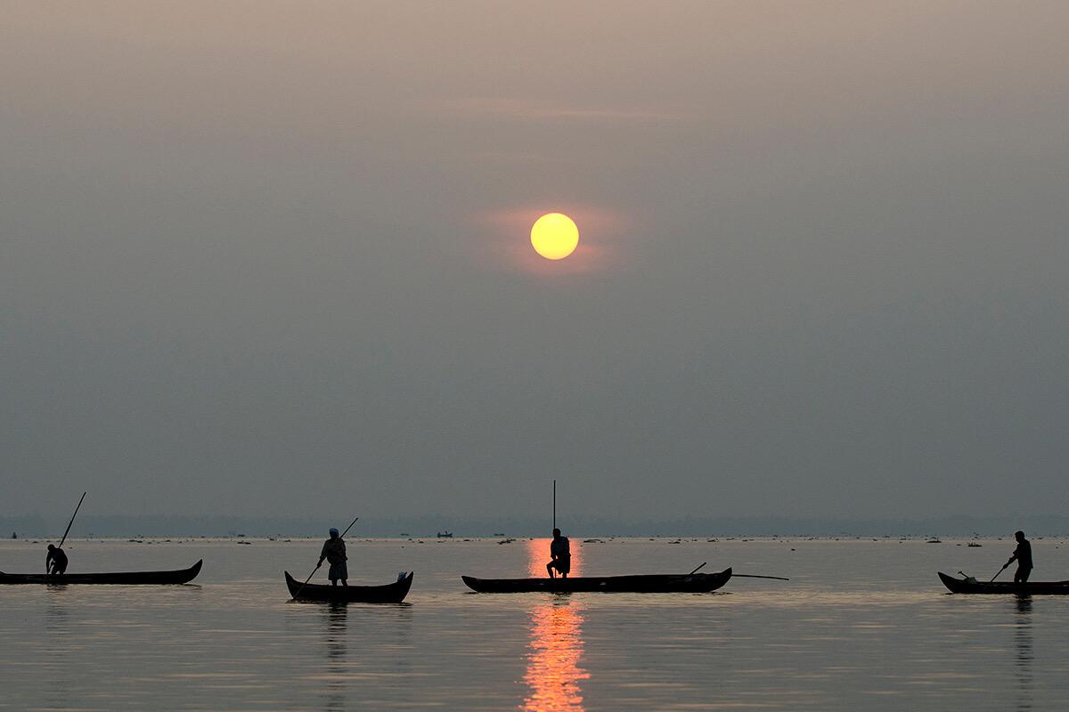 Fishing canoes silhouetted on the lake at sunset, the sun low over the water