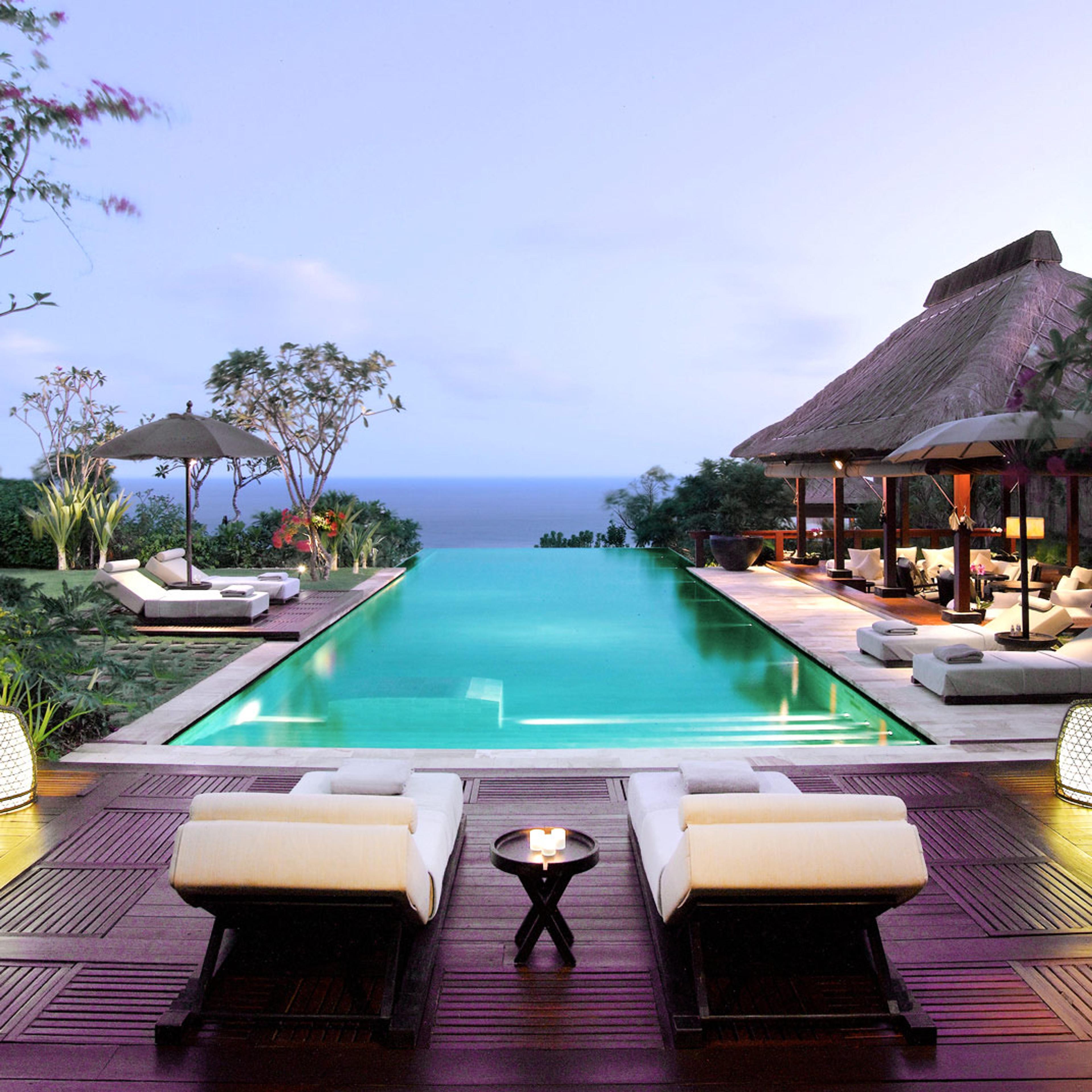 The infinity pool on the clifftop, white daybeds at its end and the sea beyond the edge