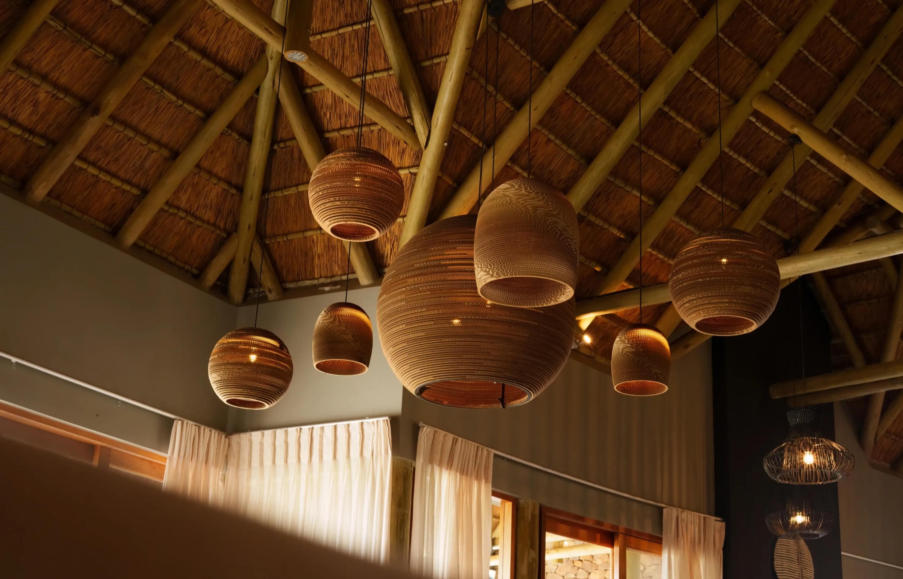 A high thatched ceiling with exposed timber poles, hung with woven pendant lamps above sheer curtains.