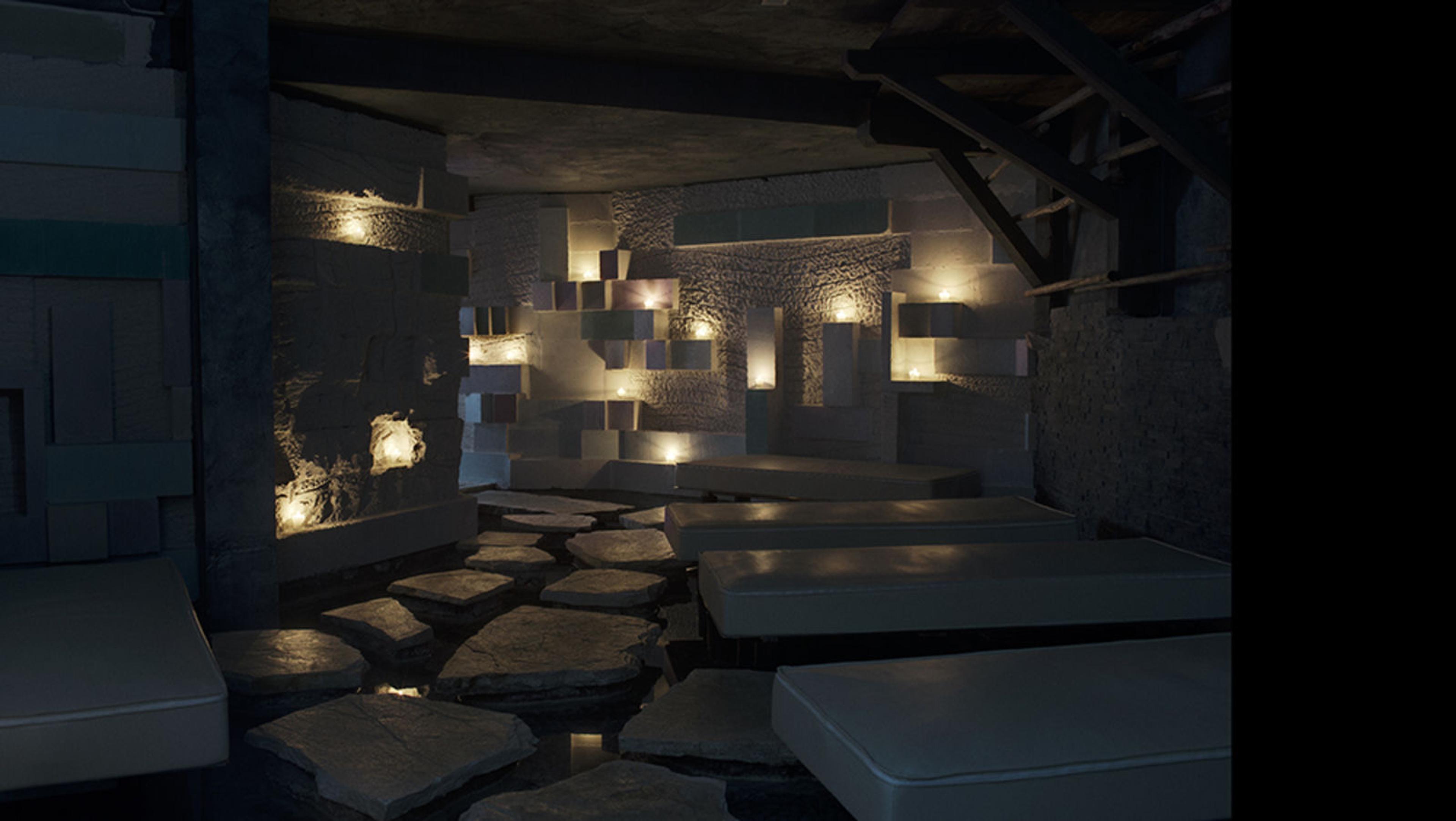 A candlelit stone lounge with low upholstered daybeds beside a shallow water channel and stepping stones.