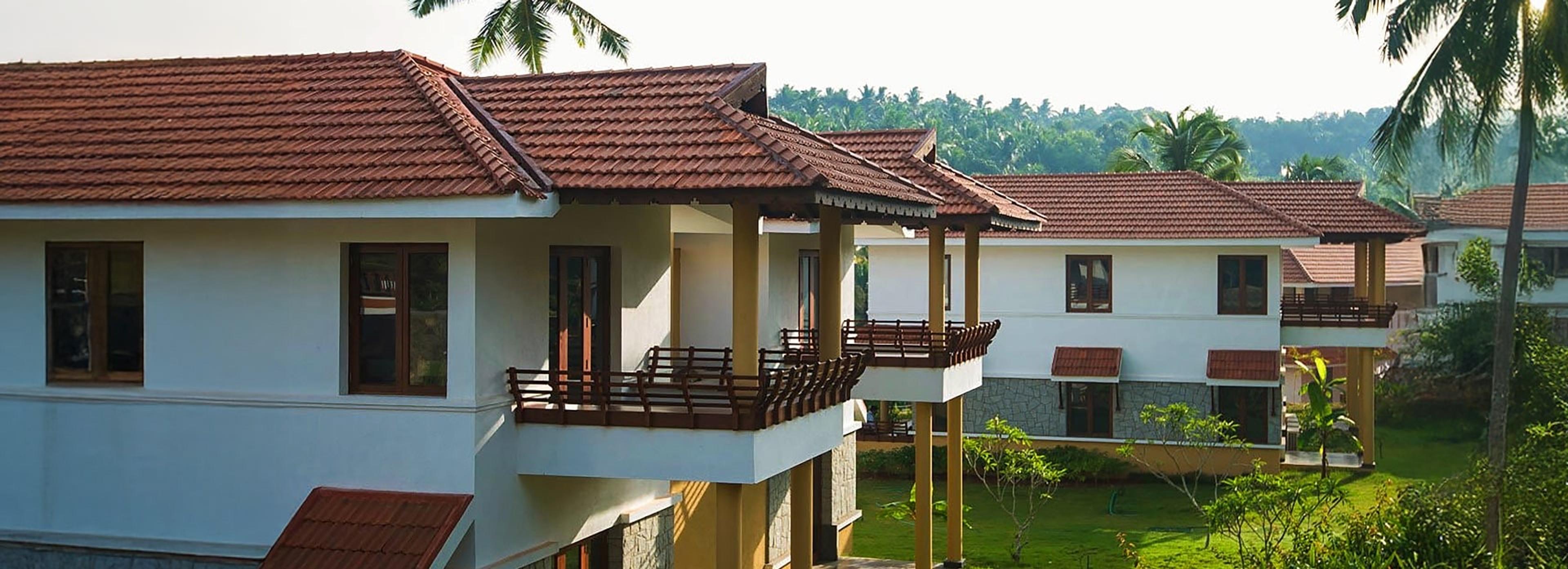 a two storey building with red tiled roofs, timber balconies and white walls, set among lawns and palm trees