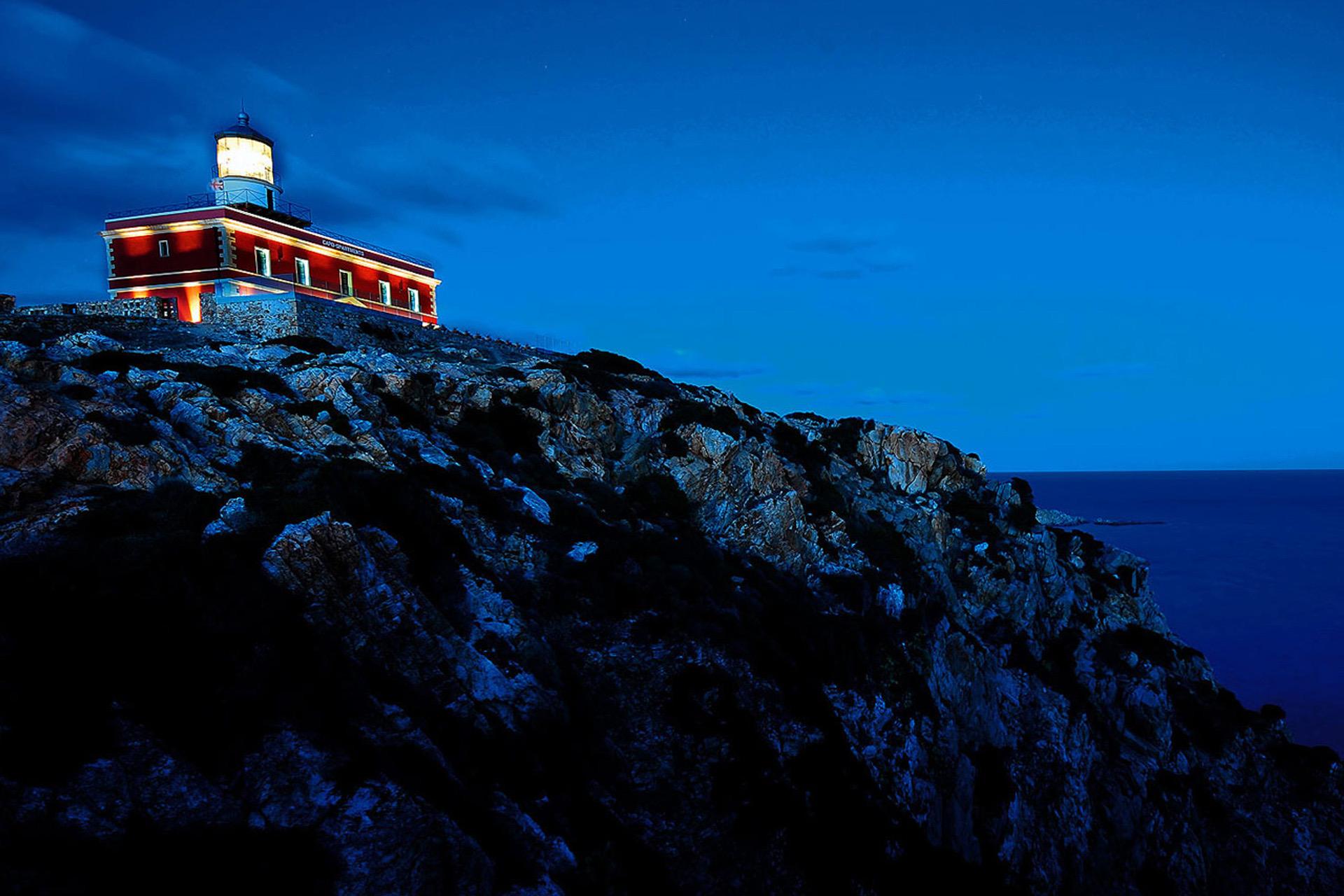 Faro Capo Spartivento's lighthouse lit at dusk on its rocky headland above the sea
