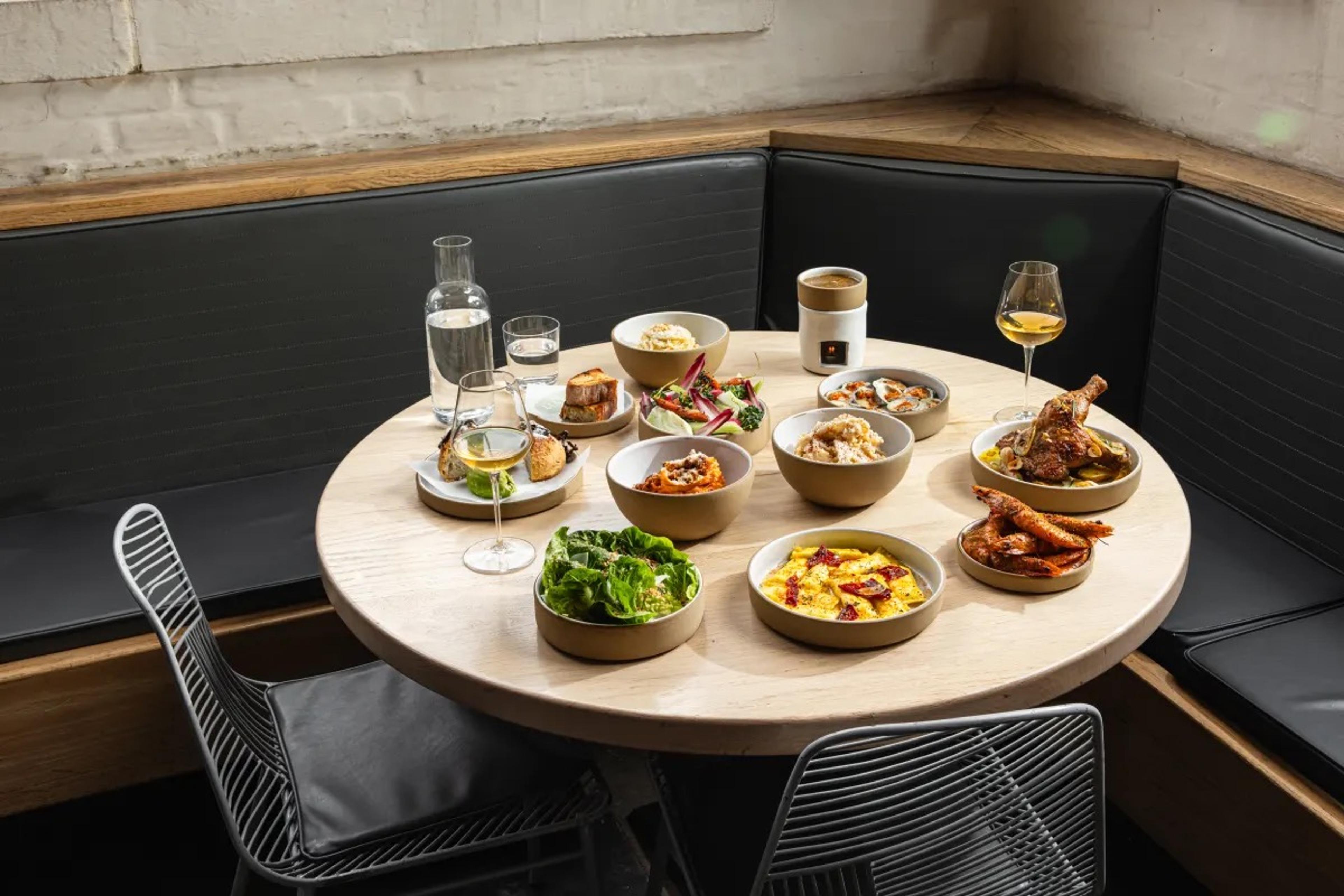 A round table laid with small plates and wine glasses beside a dark leather banquette