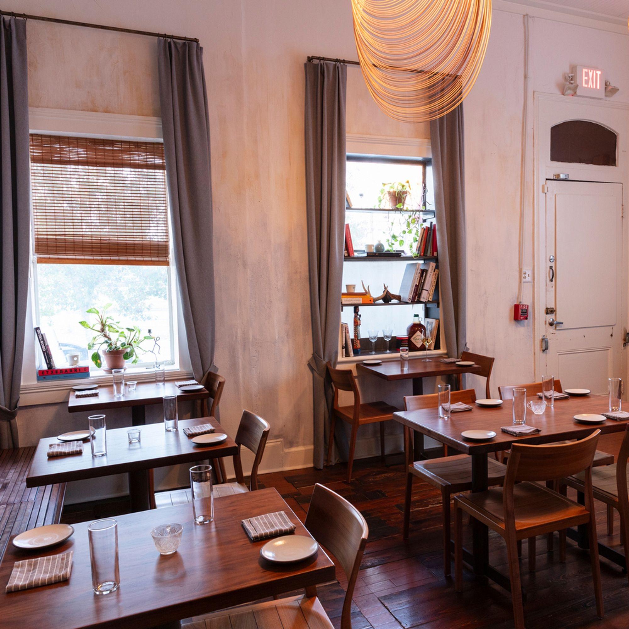 A small dining room of wooden tables, with plants in the windows
