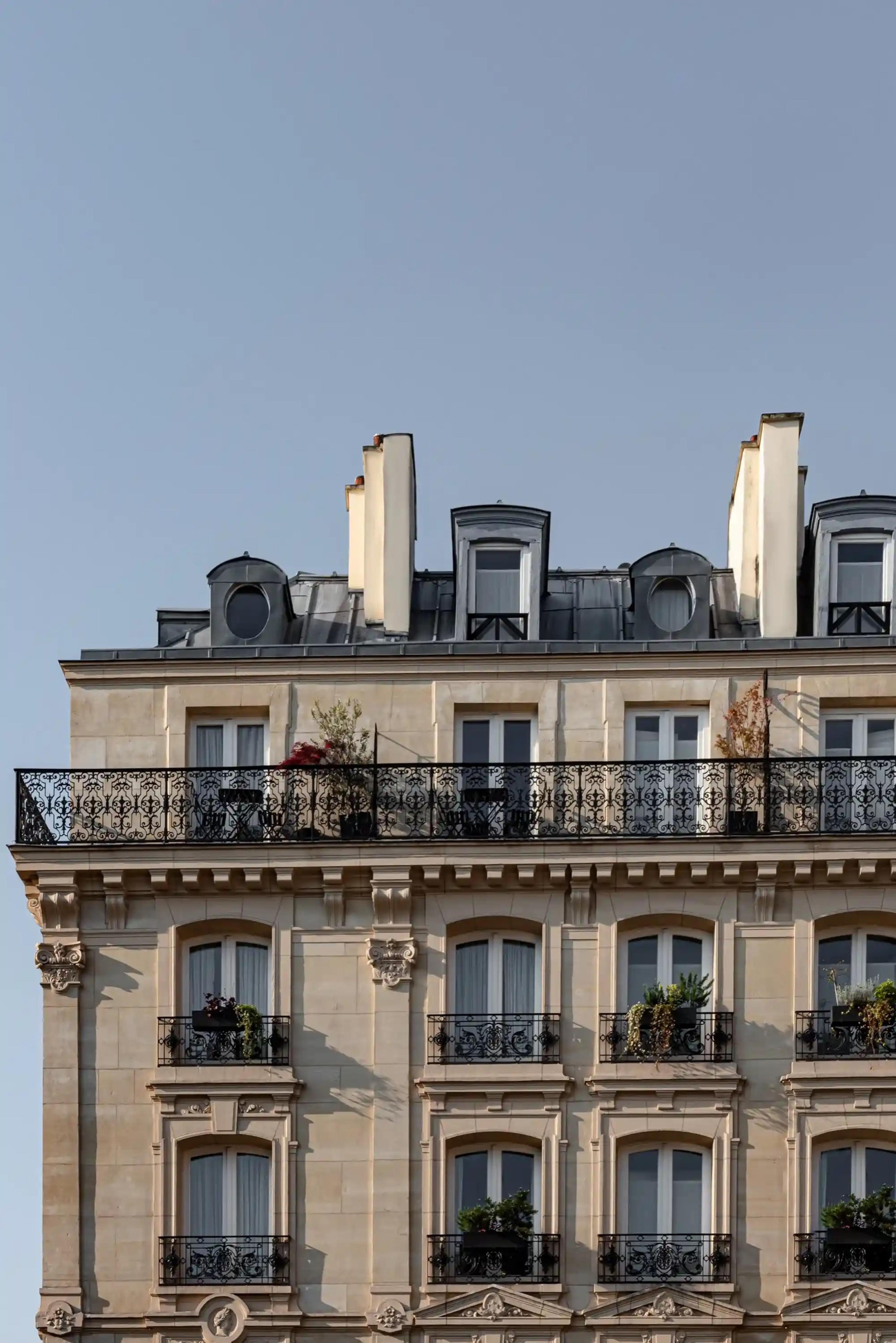The cream stone upper floors of a Haussmannian building, with wrought iron balconies, chimney pots and a clear blue sky above.