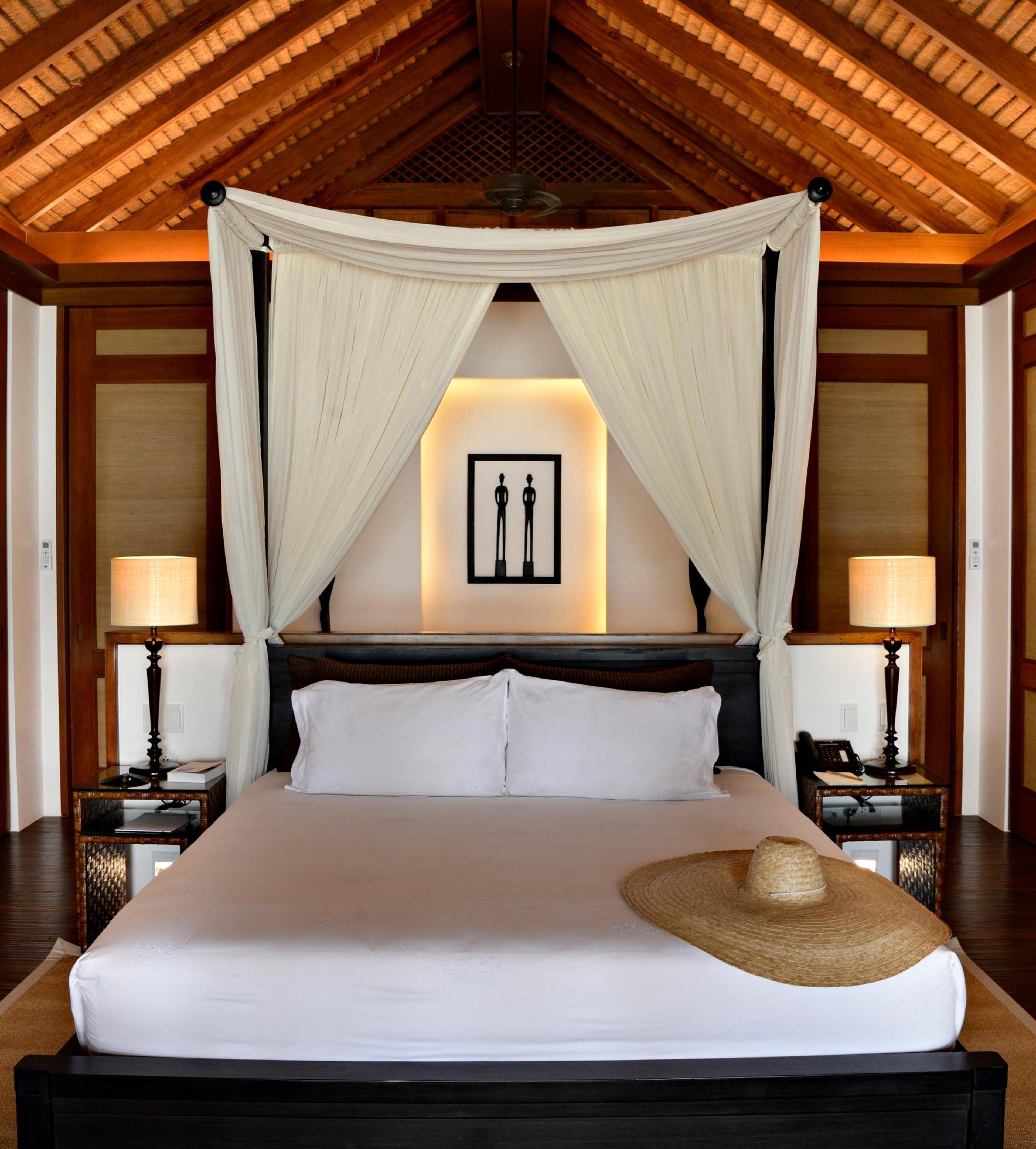 A canopied bed hung with white curtains in a timber-framed villa bedroom.