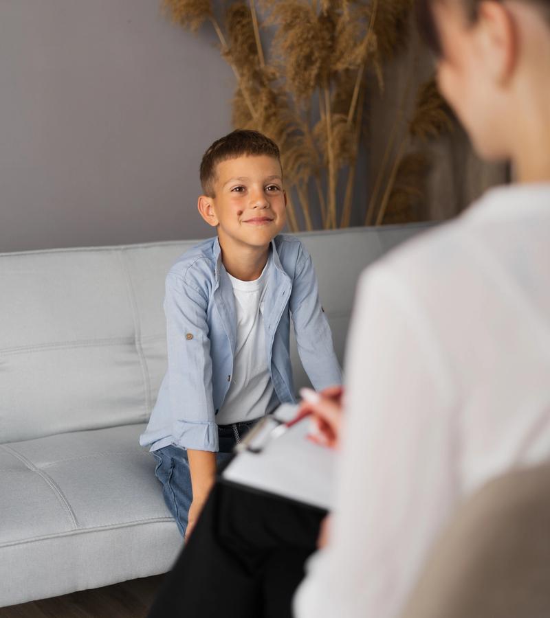 Niño sonriente sentado en un sofá hablando con una terapeuta que toma notas