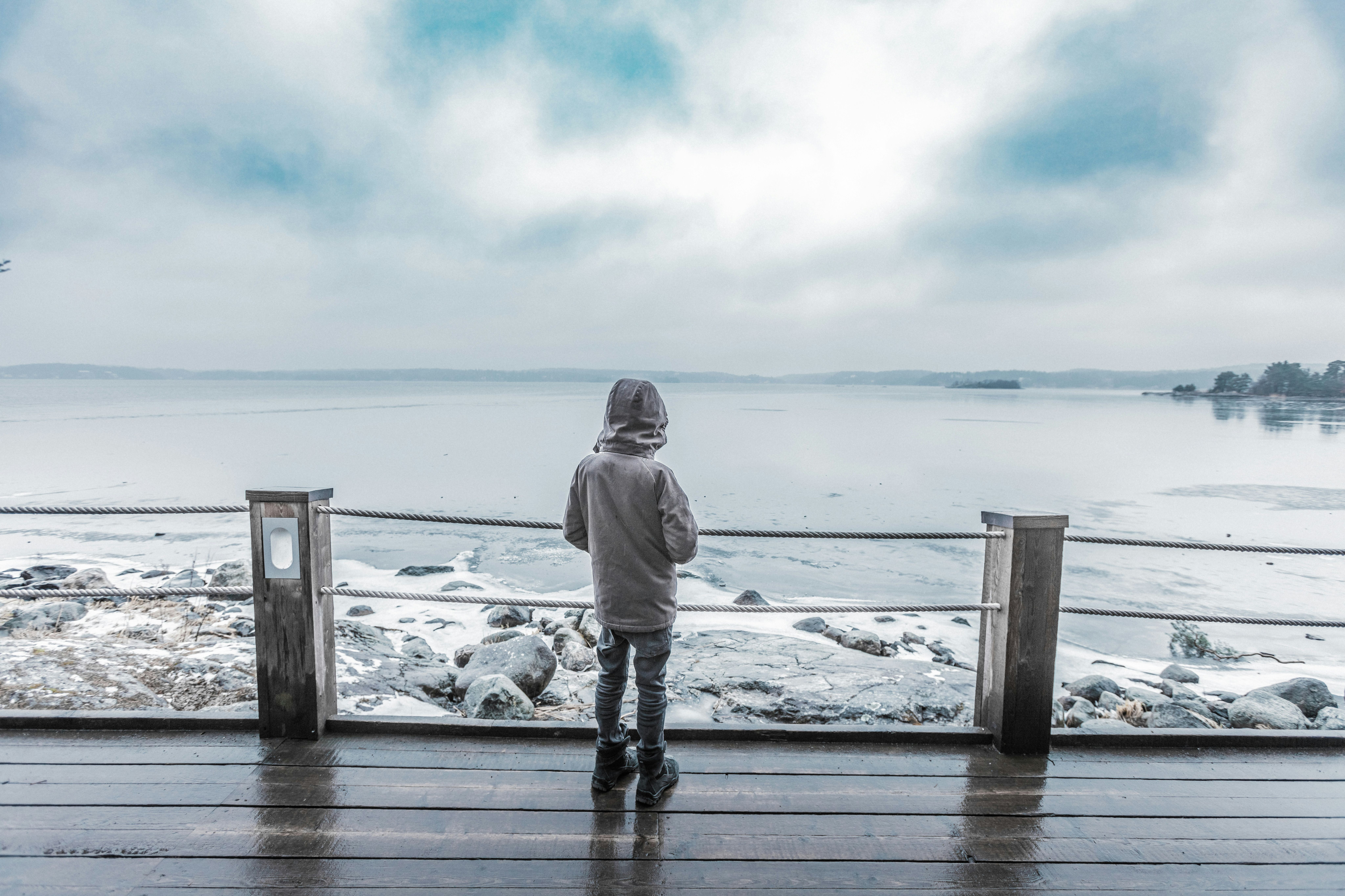 Boy in jacket overlooking beach at pier while raining.