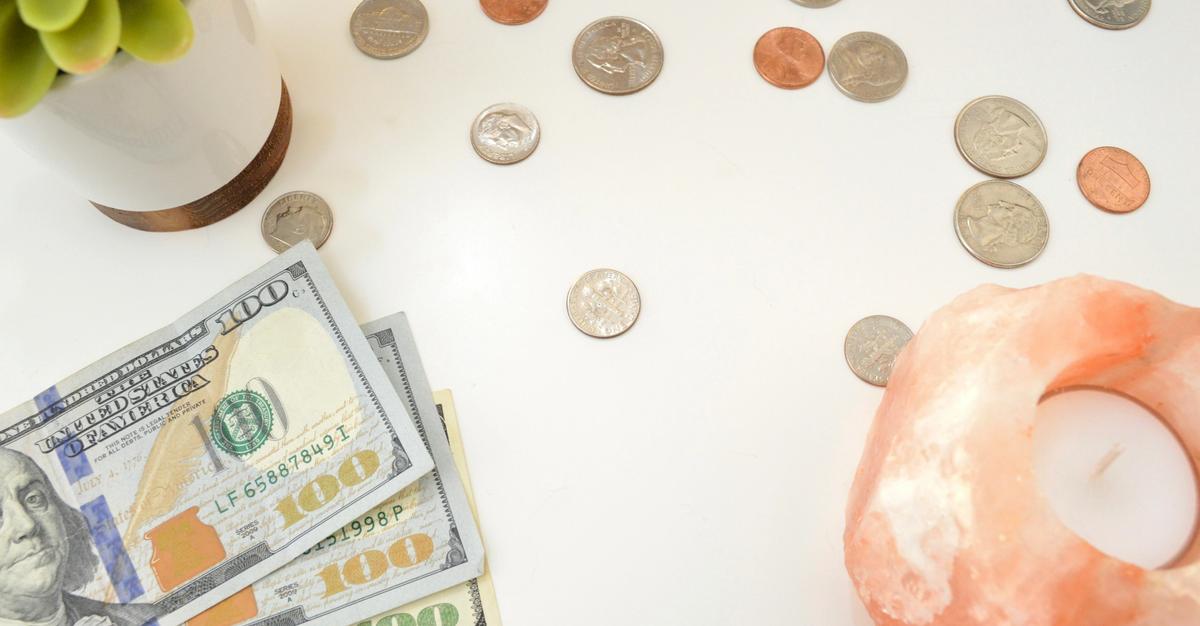 Money and change on a desk next to a candle and plant.