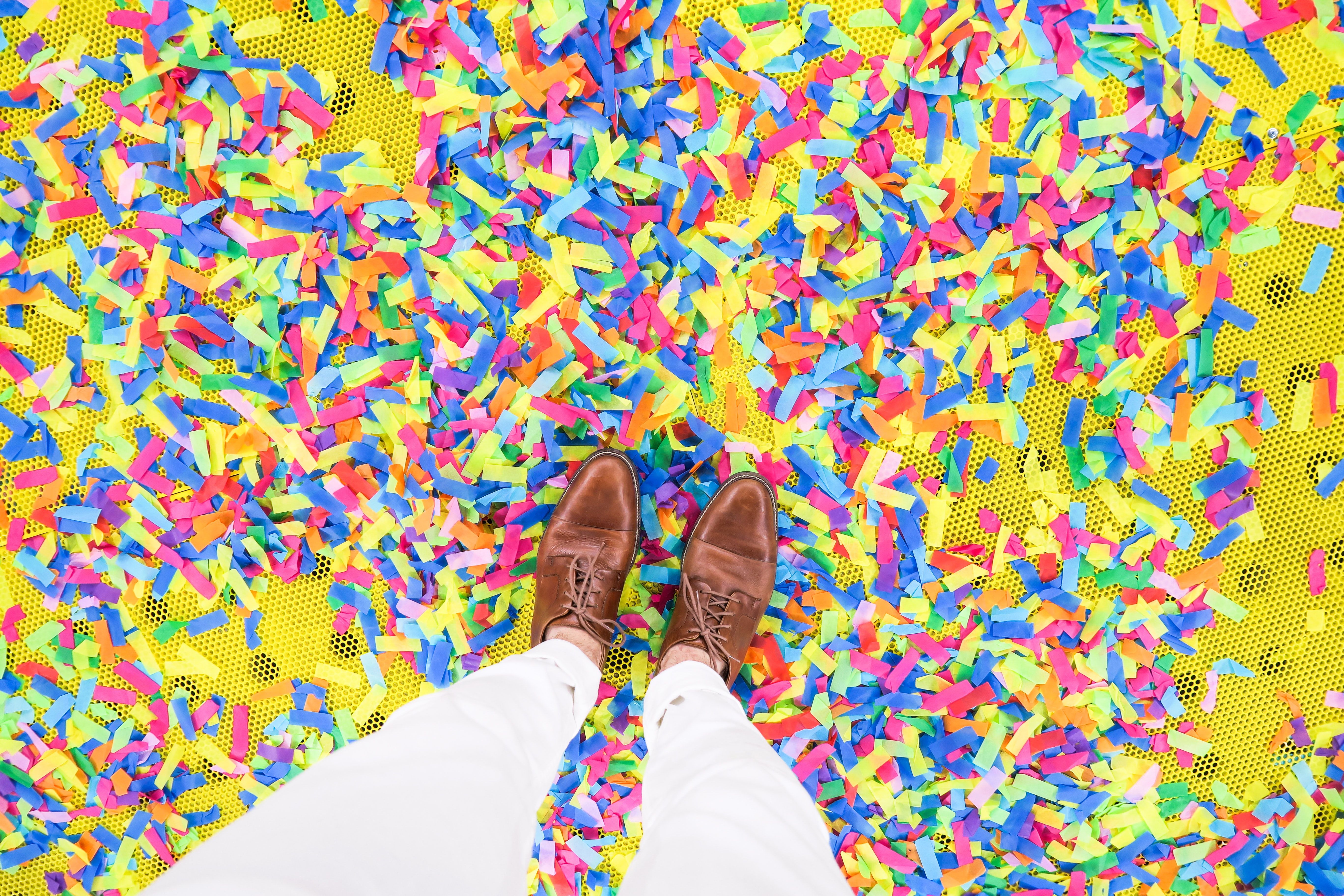 Man standing in multi-colored confetti with brown dress shoes. 