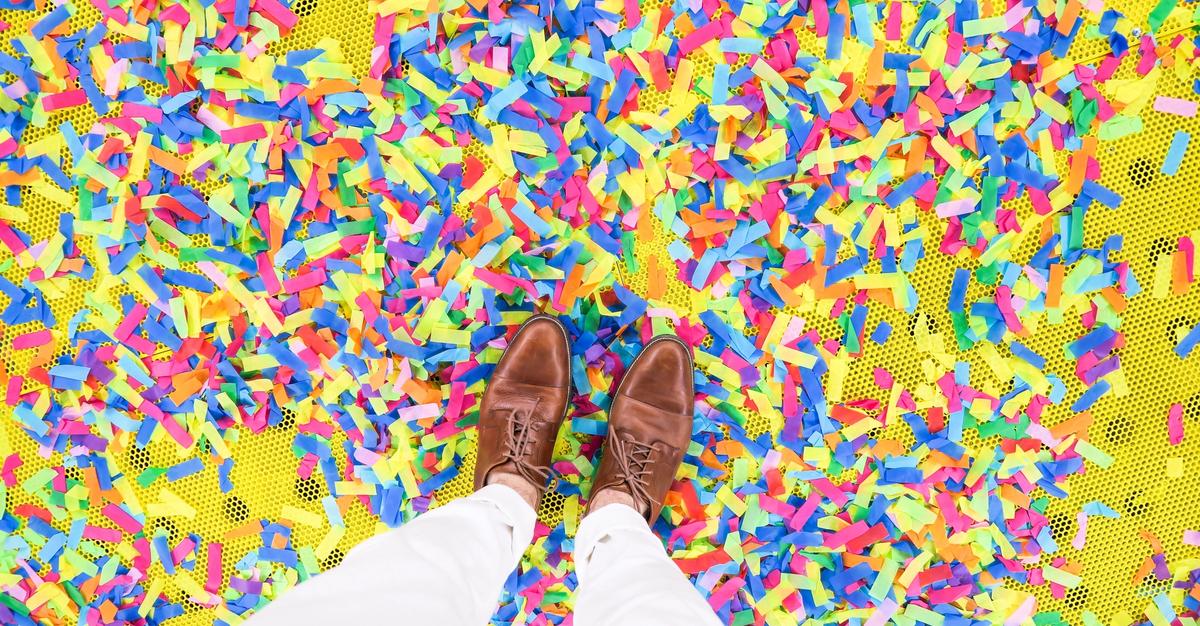 Man standing in multi-colored confetti with brown dress shoes.