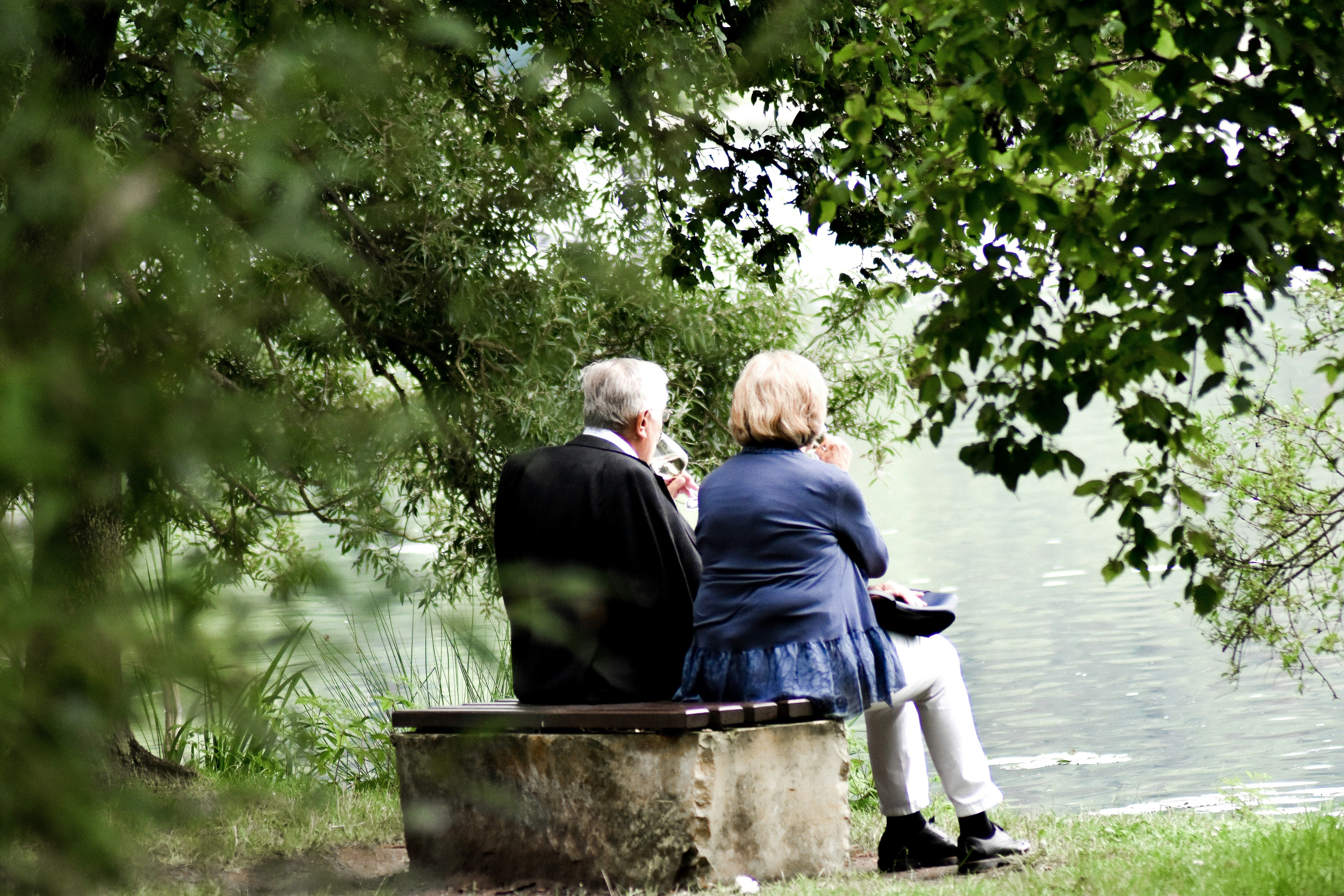 Two elderly seniors sitting on bench and sipping wine.