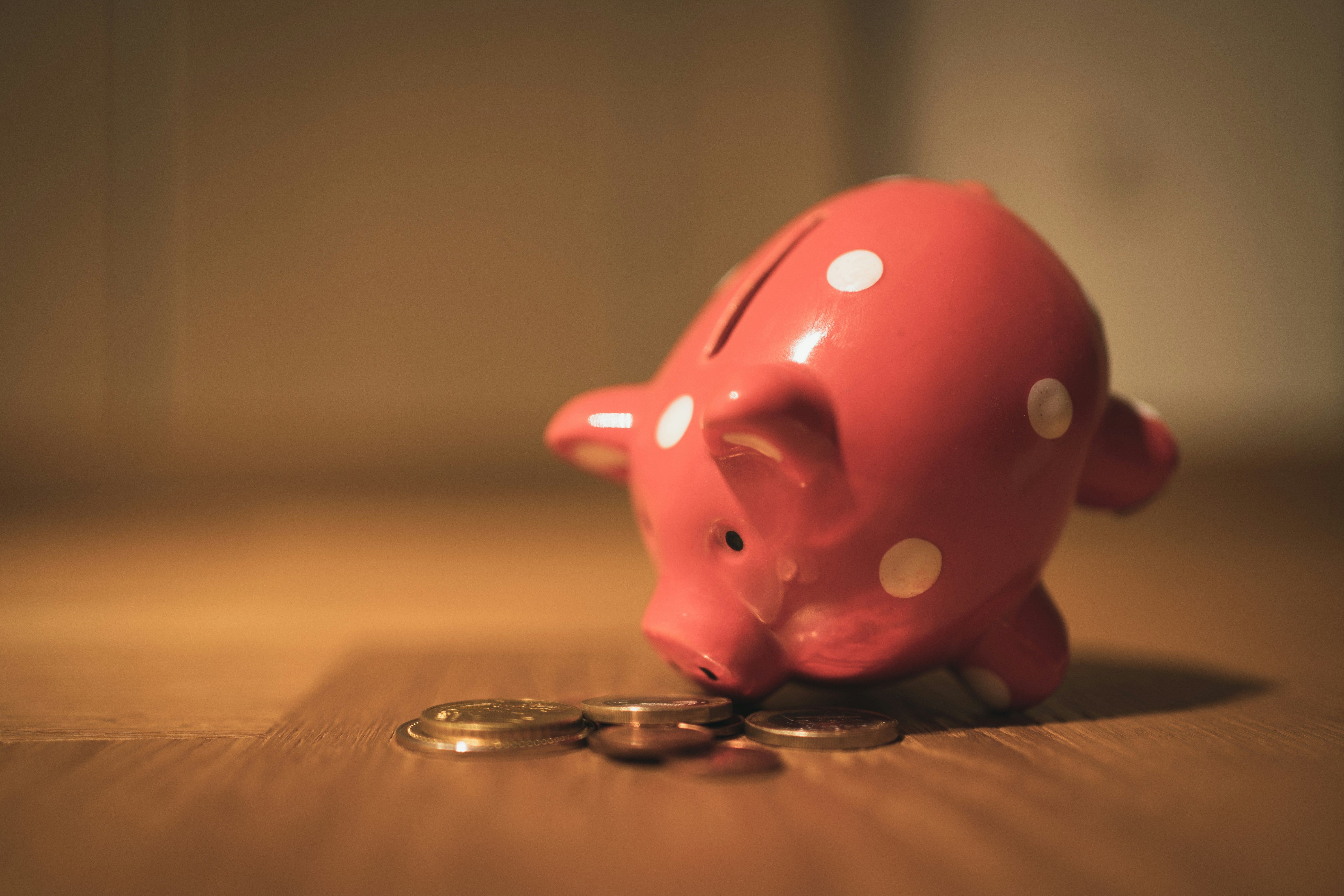 Pink piggy bank with polkadots with nose tilted towards change by Andre Taissin.