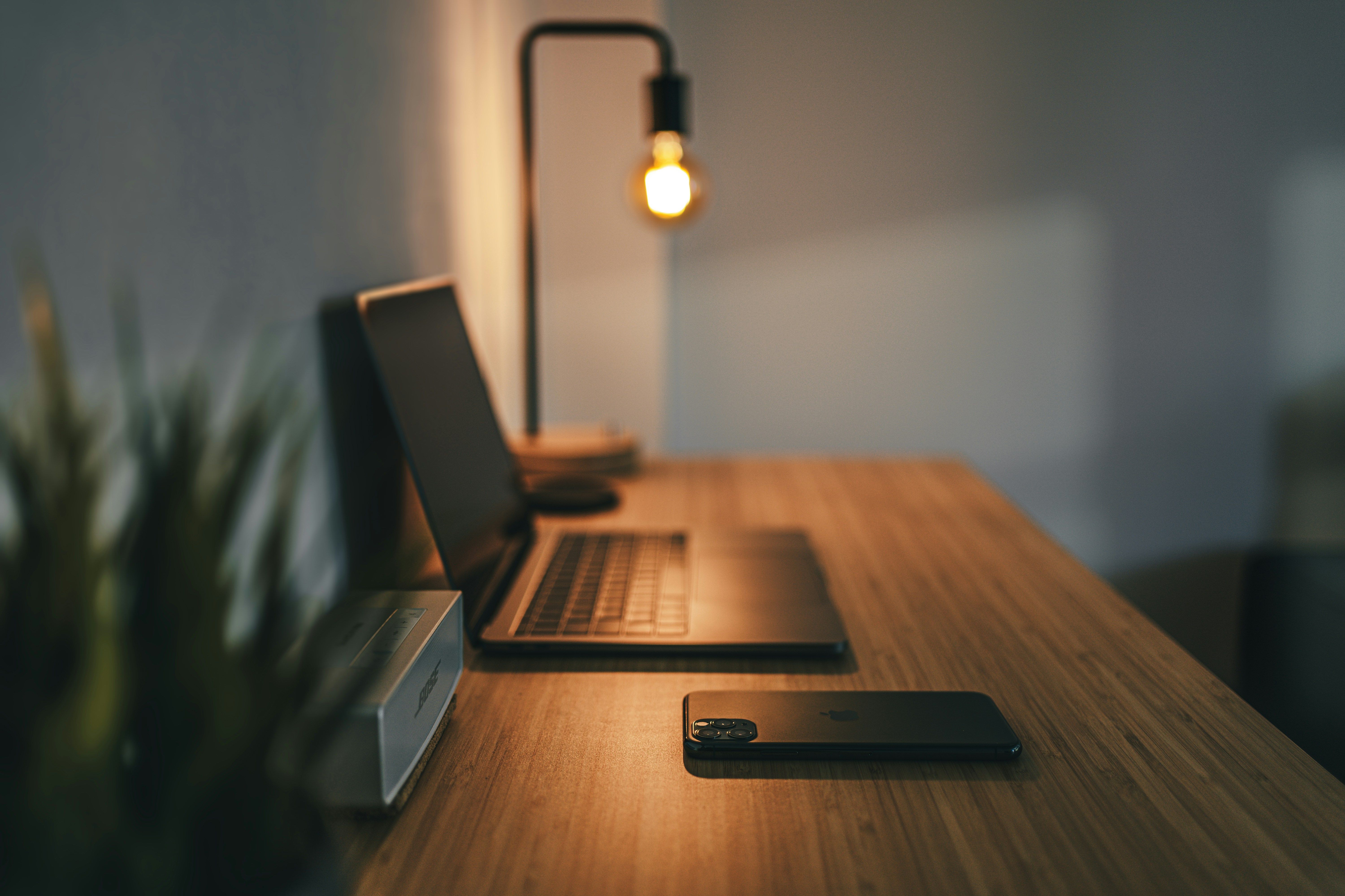 Macbook pro and iphone on a desk with a lamp.