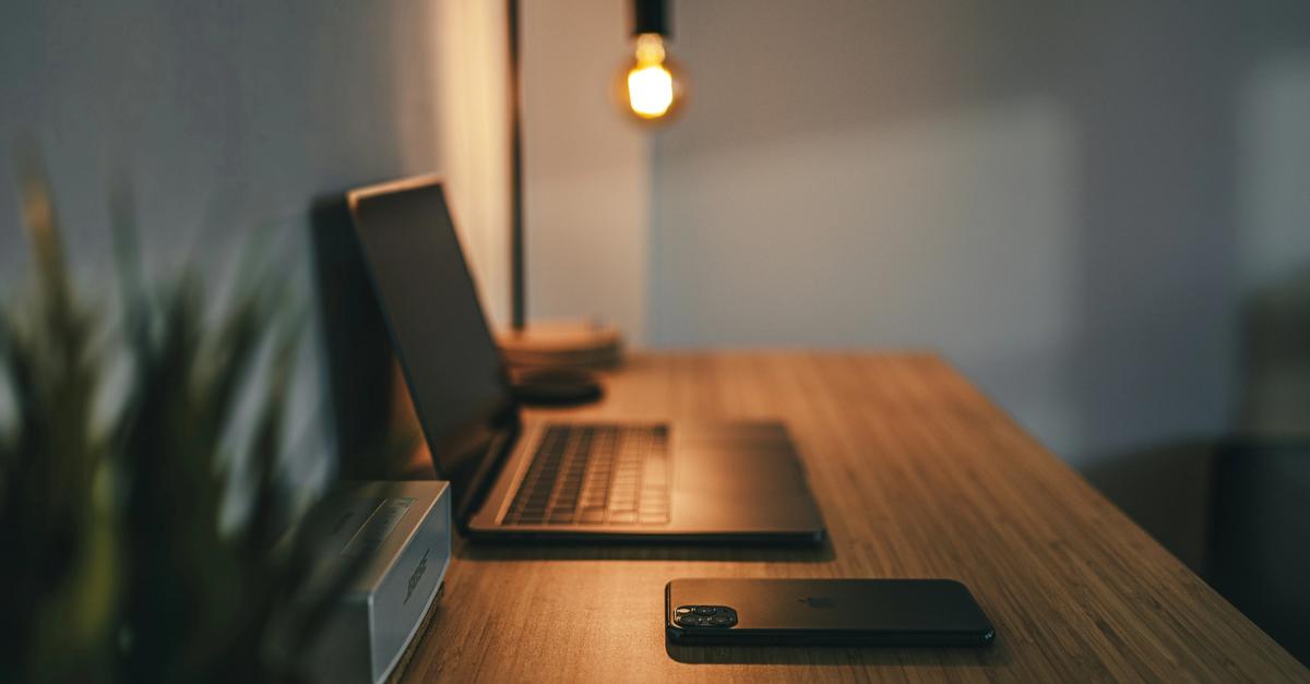 Macbook pro and iphone on a desk with a lamp.