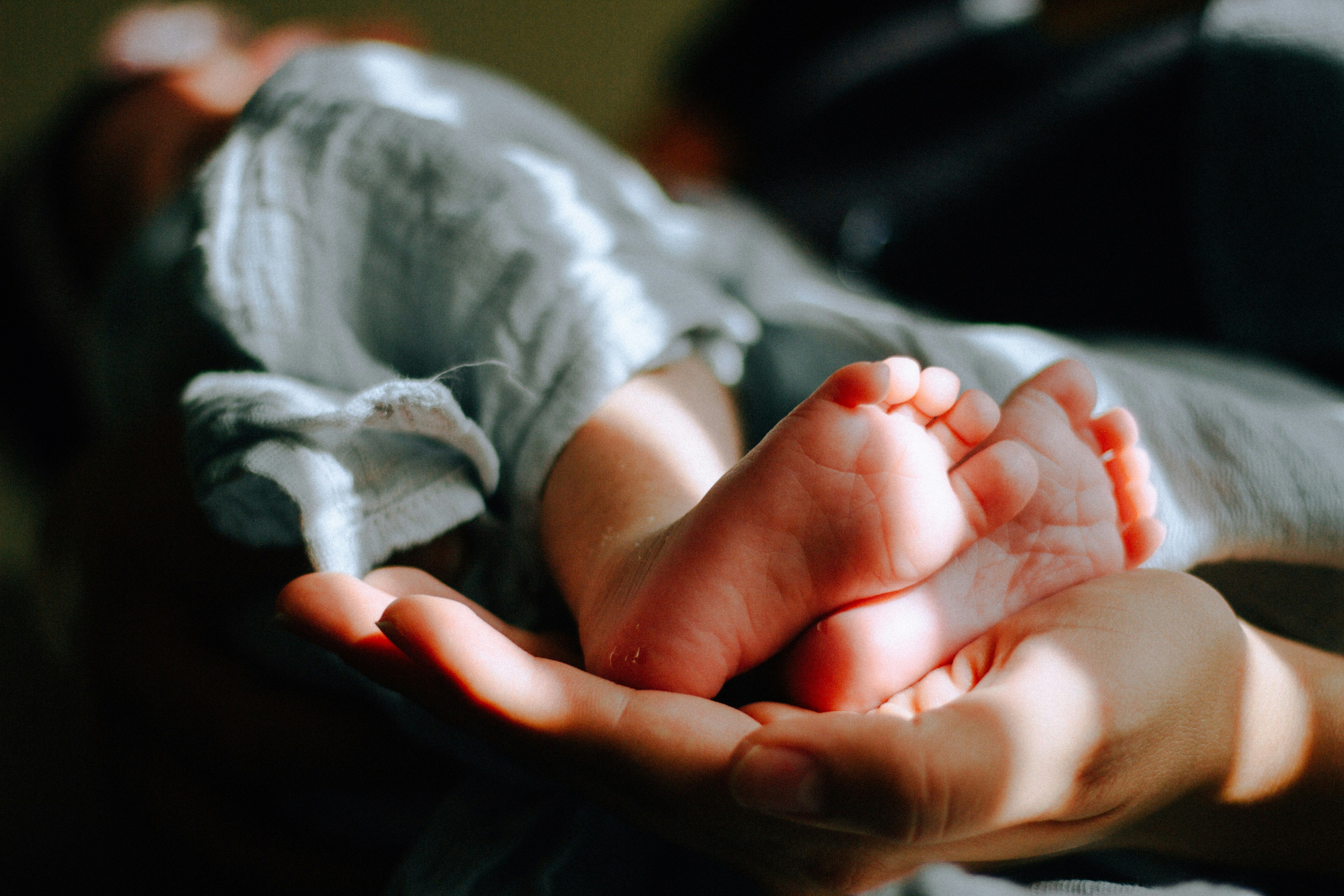 Newborn baby wrapped in a green cloth with feet sticking out.