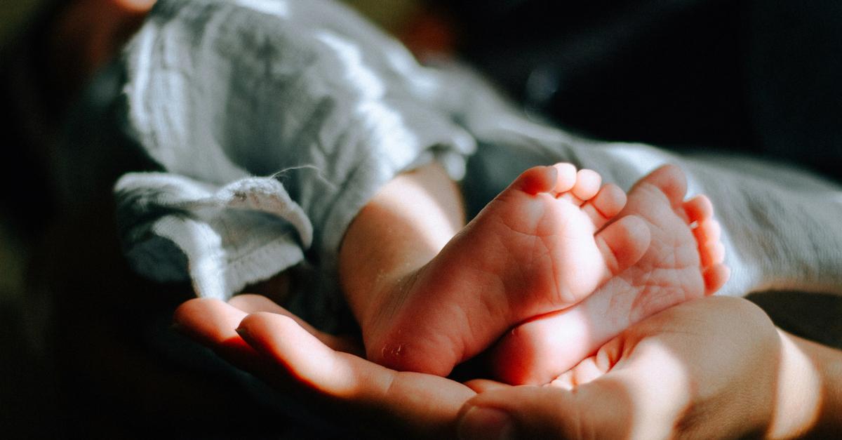 Newborn baby wrapped in a green cloth with feet sticking out.
