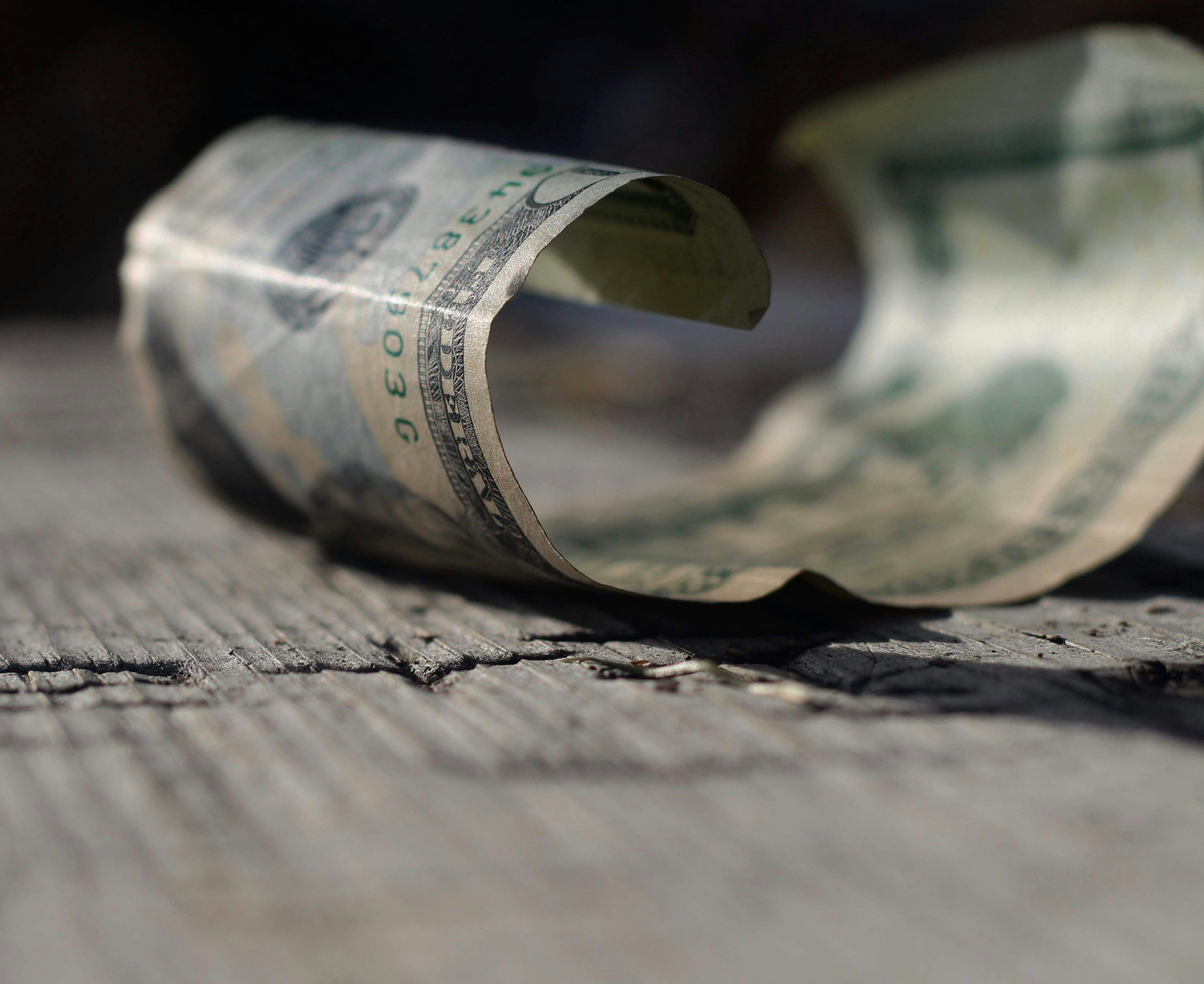 Rolled up twenty dollar bill on the cracked pavement by Joshua Hoehne.